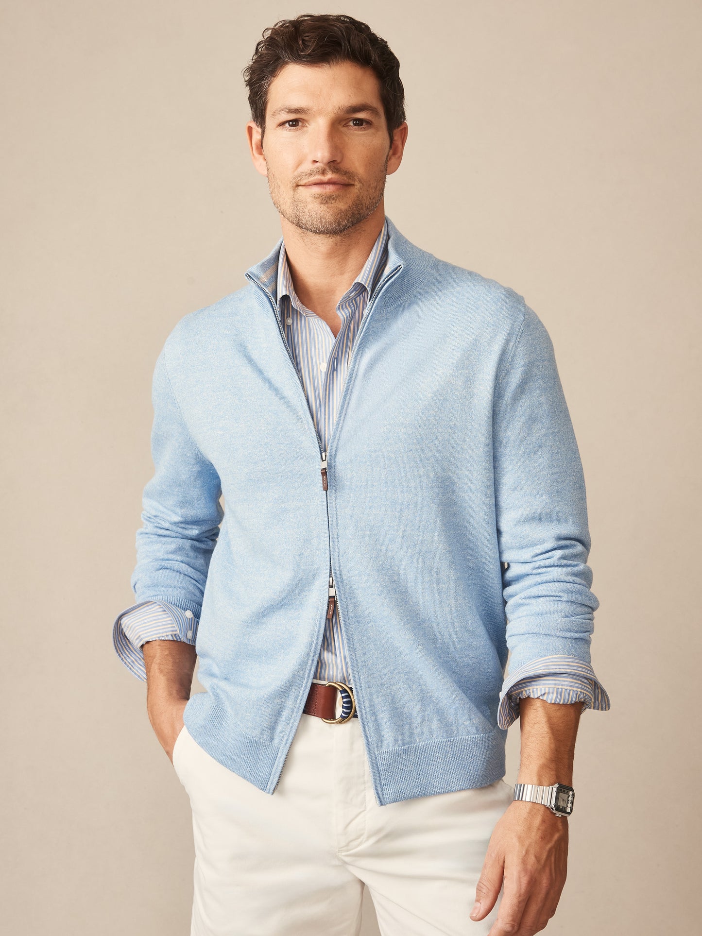 Man wearing a light blue Orwell Sweater by J.McLaughlin over a striped shirt and white pants, showcasing effortlessly stylish, enduring designs with innovative fabrics, a legacy of timeless fashion. A destination for defining style. Life, Well-Lived.