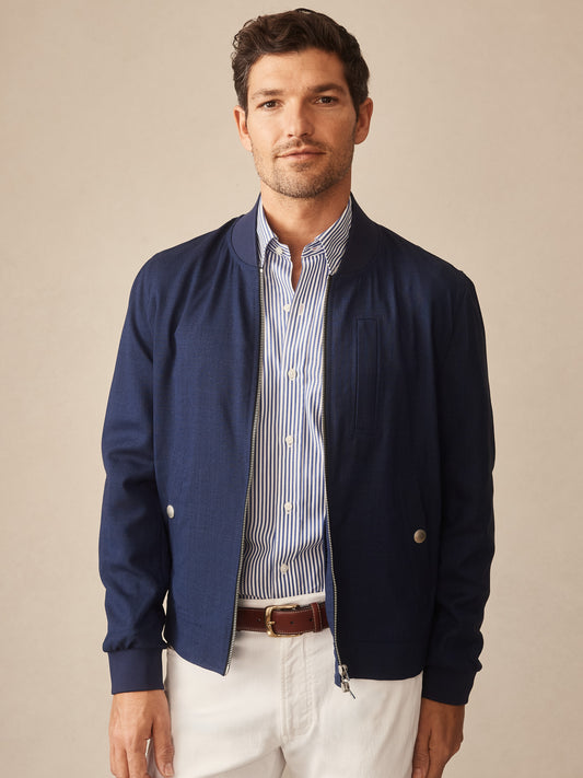 Man wearing a navy Outfield Jacket by J.McLaughlin over a striped button-up shirt and white pants, showcasing effortlessly stylish, enduring designs with innovative fabrics and a legacy of timeless fashion. A destination for defining style. Life, Well-Lived.