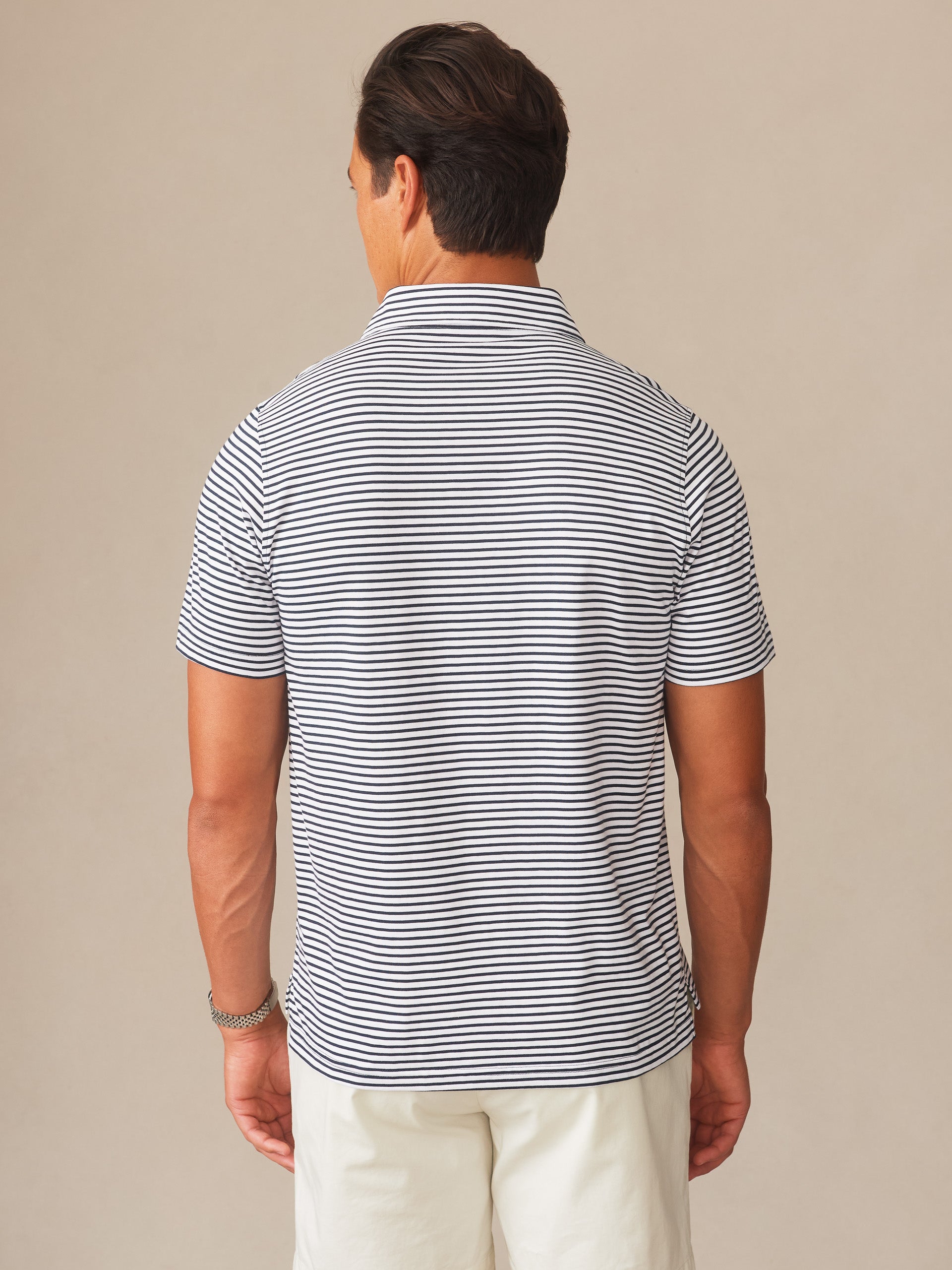 A man wearing the Owens Polo in Feeder Stripe by J.McLaughlin, featuring effortlessly stylish navy and white stripes in an enduring design crafted from innovative fabrics. A destination for defining style. Life, Well-Lived.