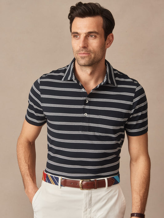 Man wearing Owens Polo in Triple Stripes by J.McLaughlin, featuring navy and white horizontal stripes, styled with a colorful belt and white pants, showcasing effortlessly stylish, enduring designs with innovative fabrics. A destination for defining style. Life, Well-Lived.