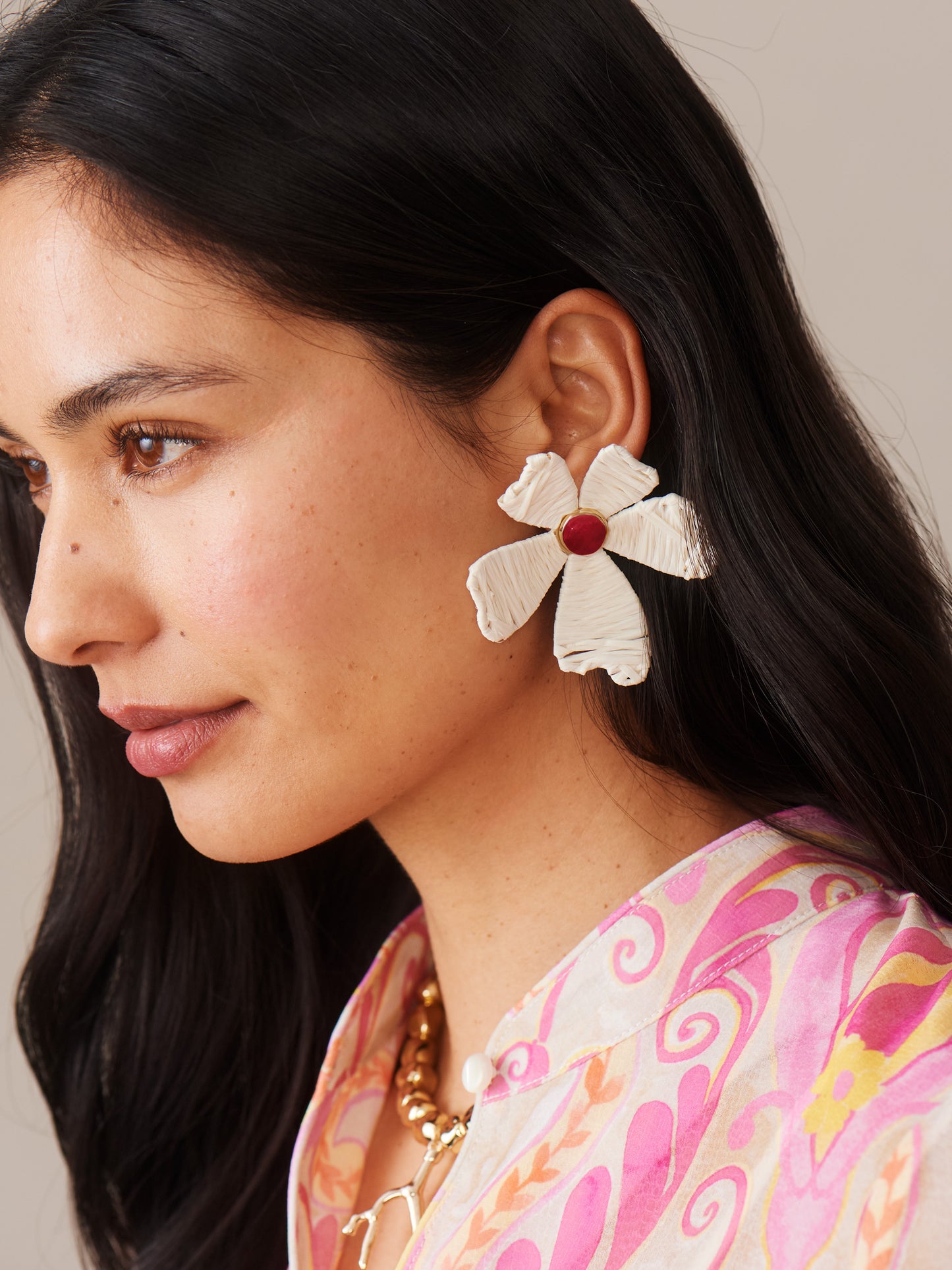 Close-up of a woman wearing cream-colored Flower Earrings by J.McLaughlin paired with a pink patterned blouse, showcasing effortlessly stylish, enduring designs in a legacy of timeless fashion.