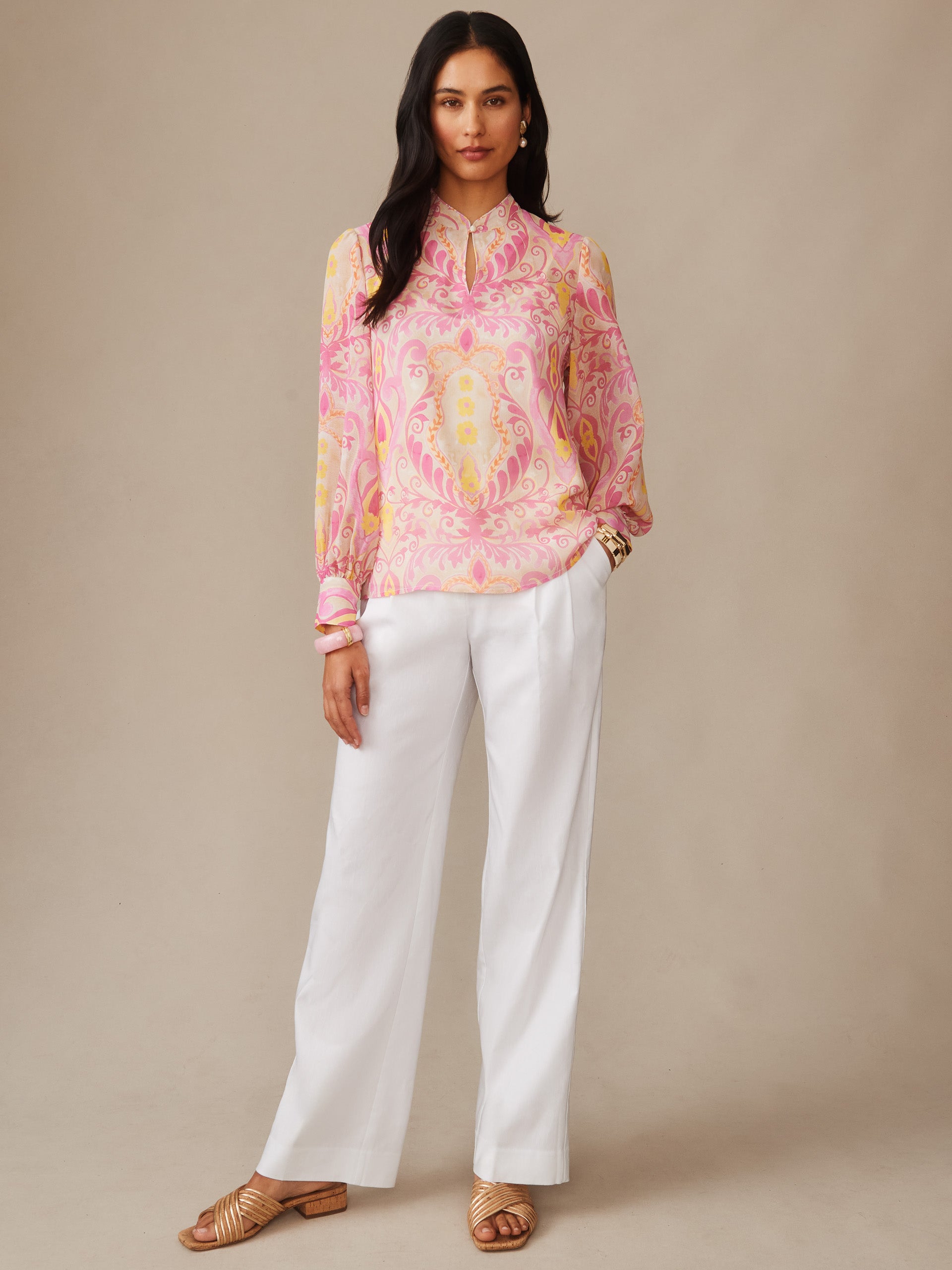 Woman wearing Peyton Blouse in Mini Deco Bloom by J.McLaughlin in soft pink and cream with white wide-leg pants, showcasing effortlessly stylish, enduring designs for a life well-lived.