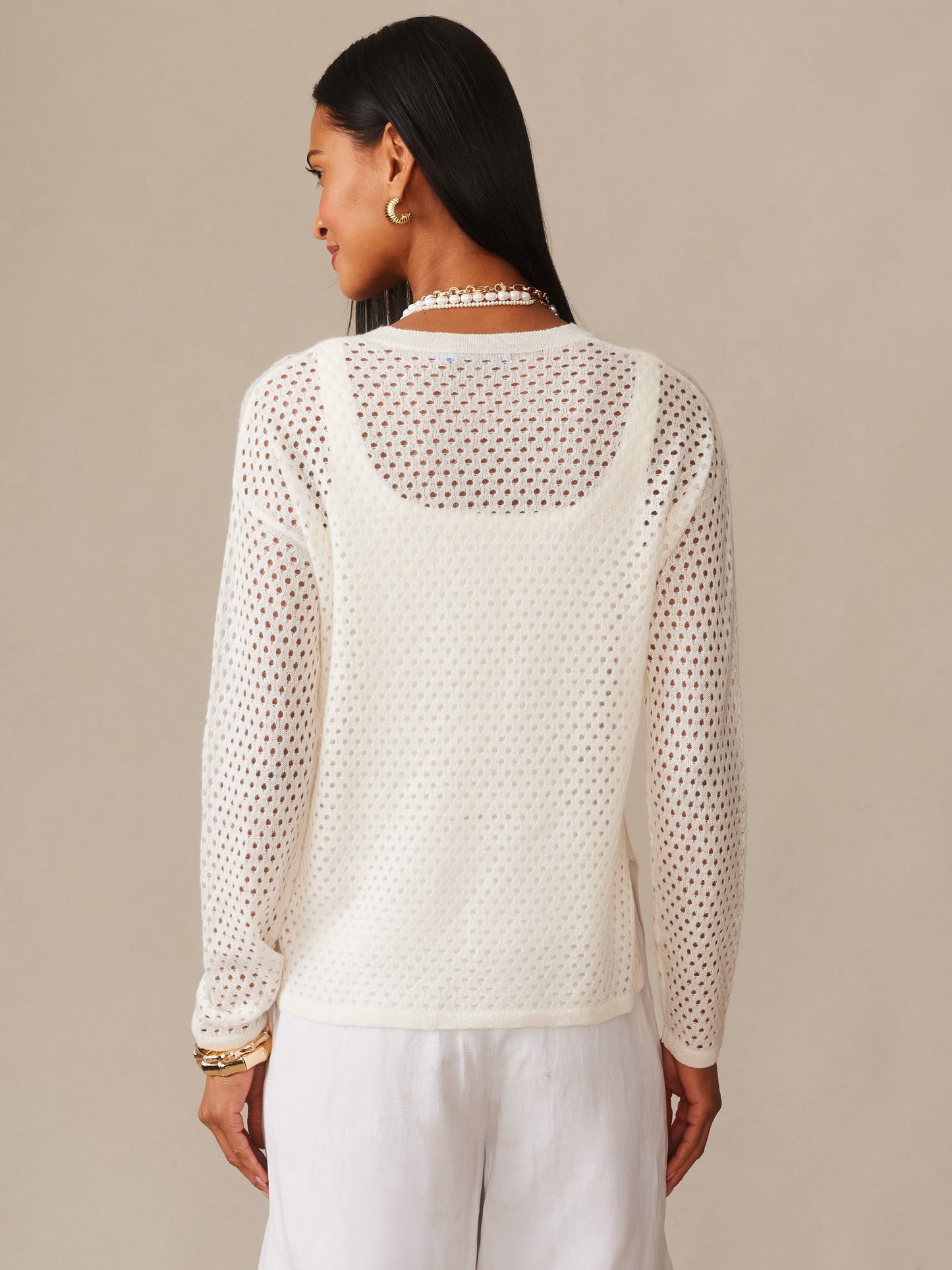 Woman wearing a white Philomena Cashmere Linen Sweater by J.McLaughlin, featuring an open-knit design layered over a camisole, paired with white pants, showcasing effortlessly stylish, enduring designs with innovative fabrics for a life well-lived.
