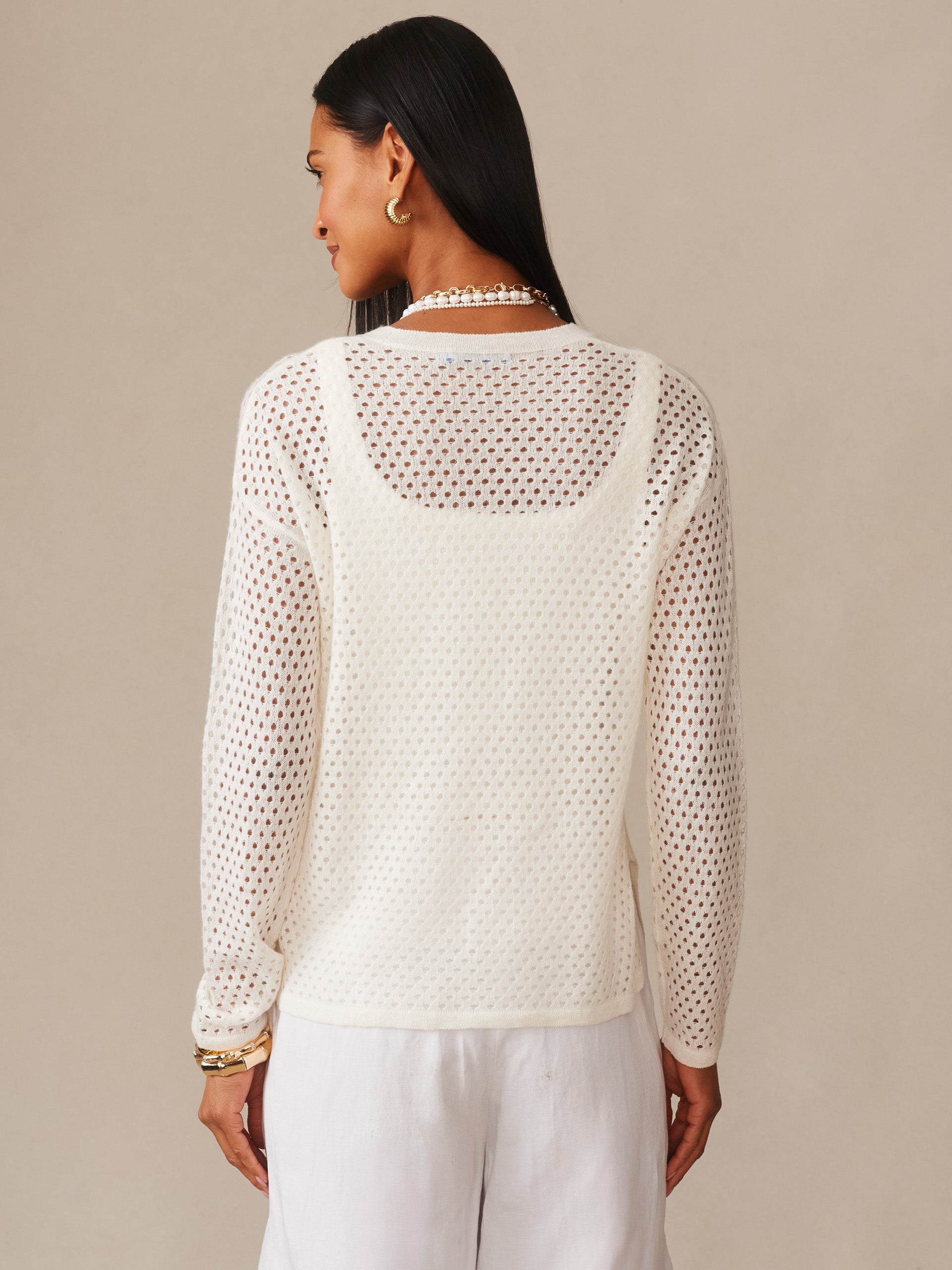 Woman wearing a white Philomena Cashmere Linen Sweater by J.McLaughlin, featuring an open-knit design layered over a camisole, paired with white pants, showcasing effortlessly stylish, enduring designs with innovative fabrics for a life well-lived.