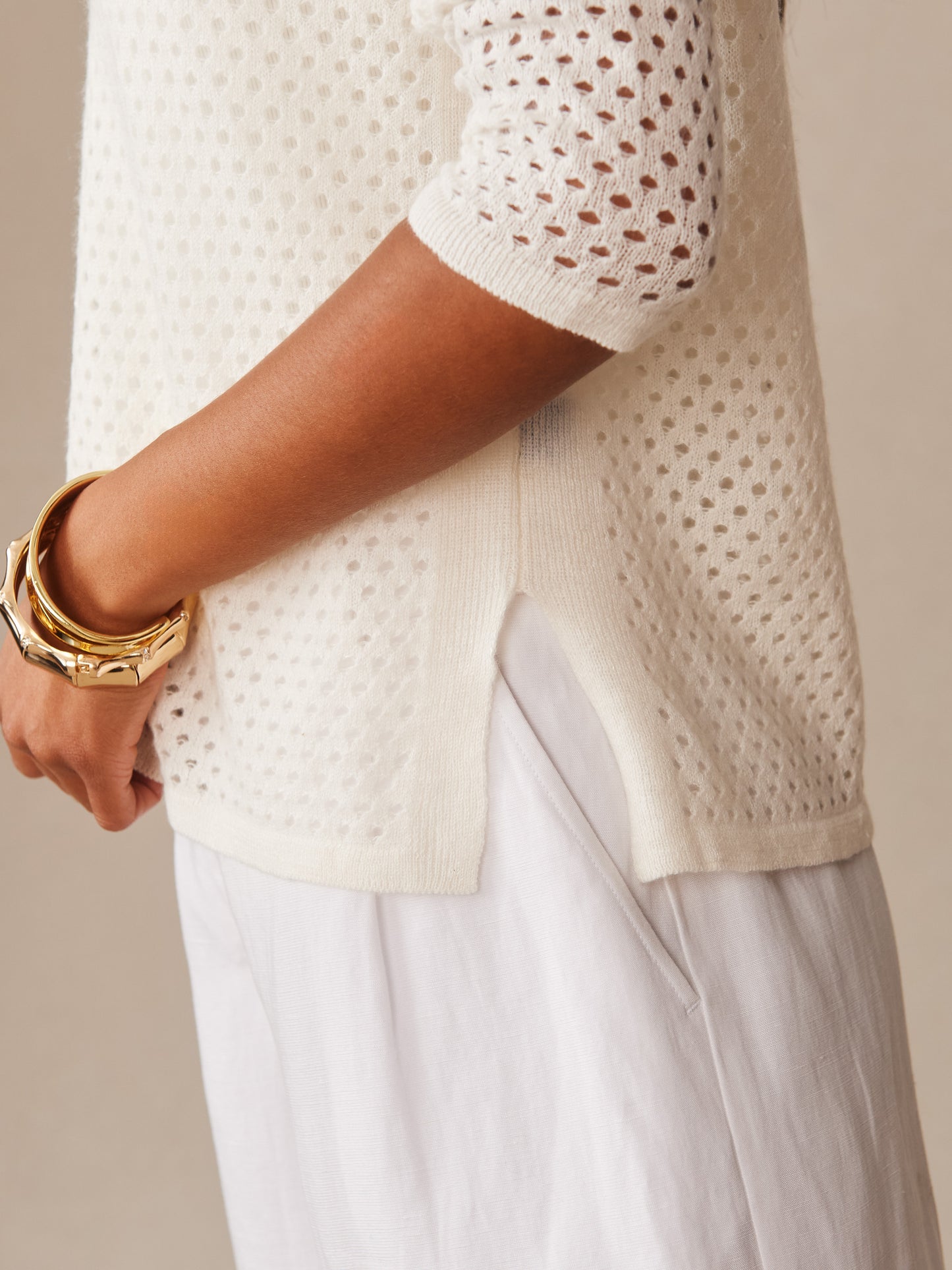 Close-up of a white Philomena Cashmere Linen Sweater by J.McLaughlin featuring open-knit sleeves and side slit, embodying effortlessly stylish, enduring designs and innovative fabrics.
