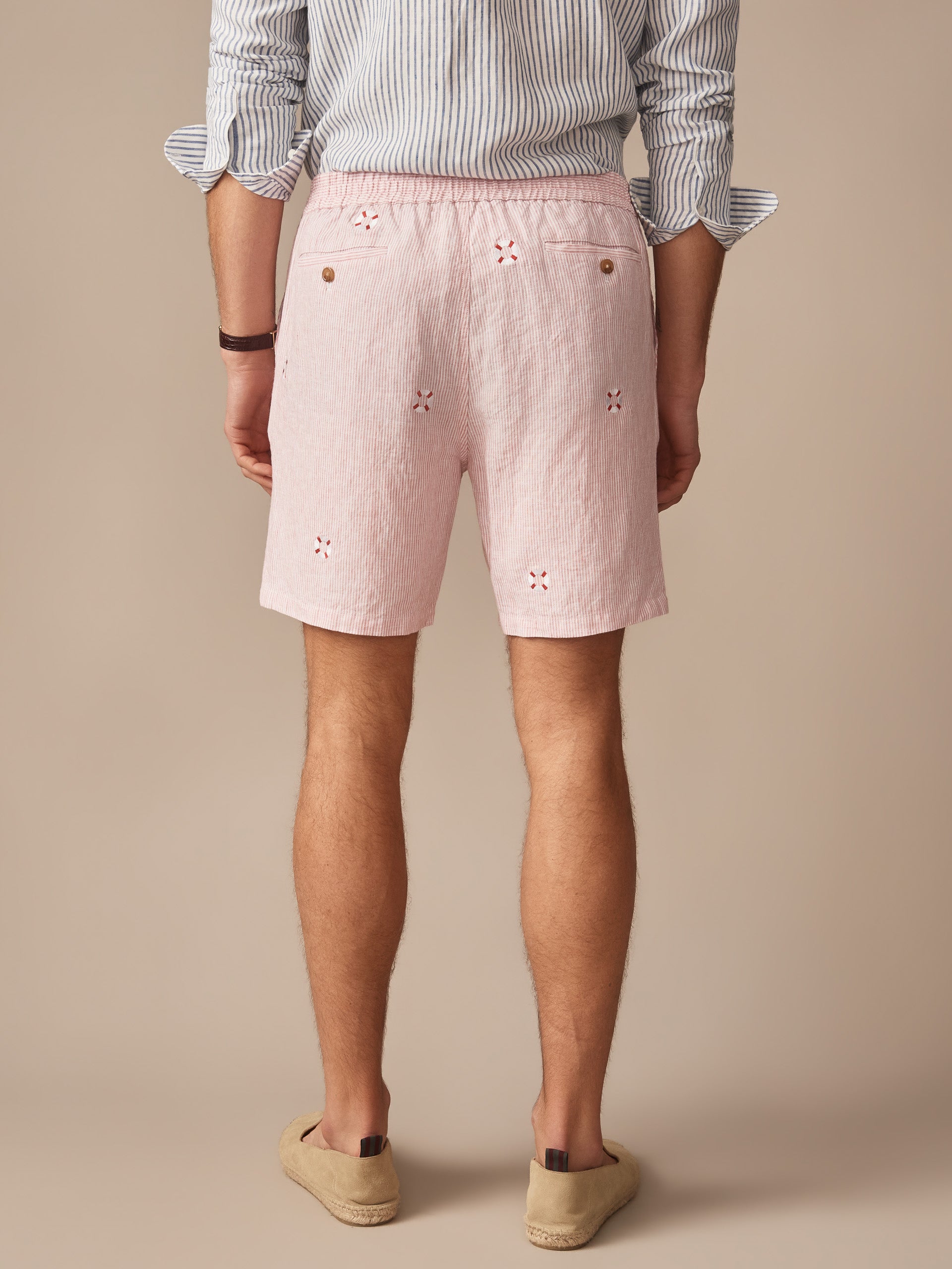 Men's back view wearing pink lightweight Newport Linen Shorts in Lifesaver by J.McLaughlin, paired with a striped shirt and casual slip-on shoes, embodying effortlessly stylish, enduring designs.