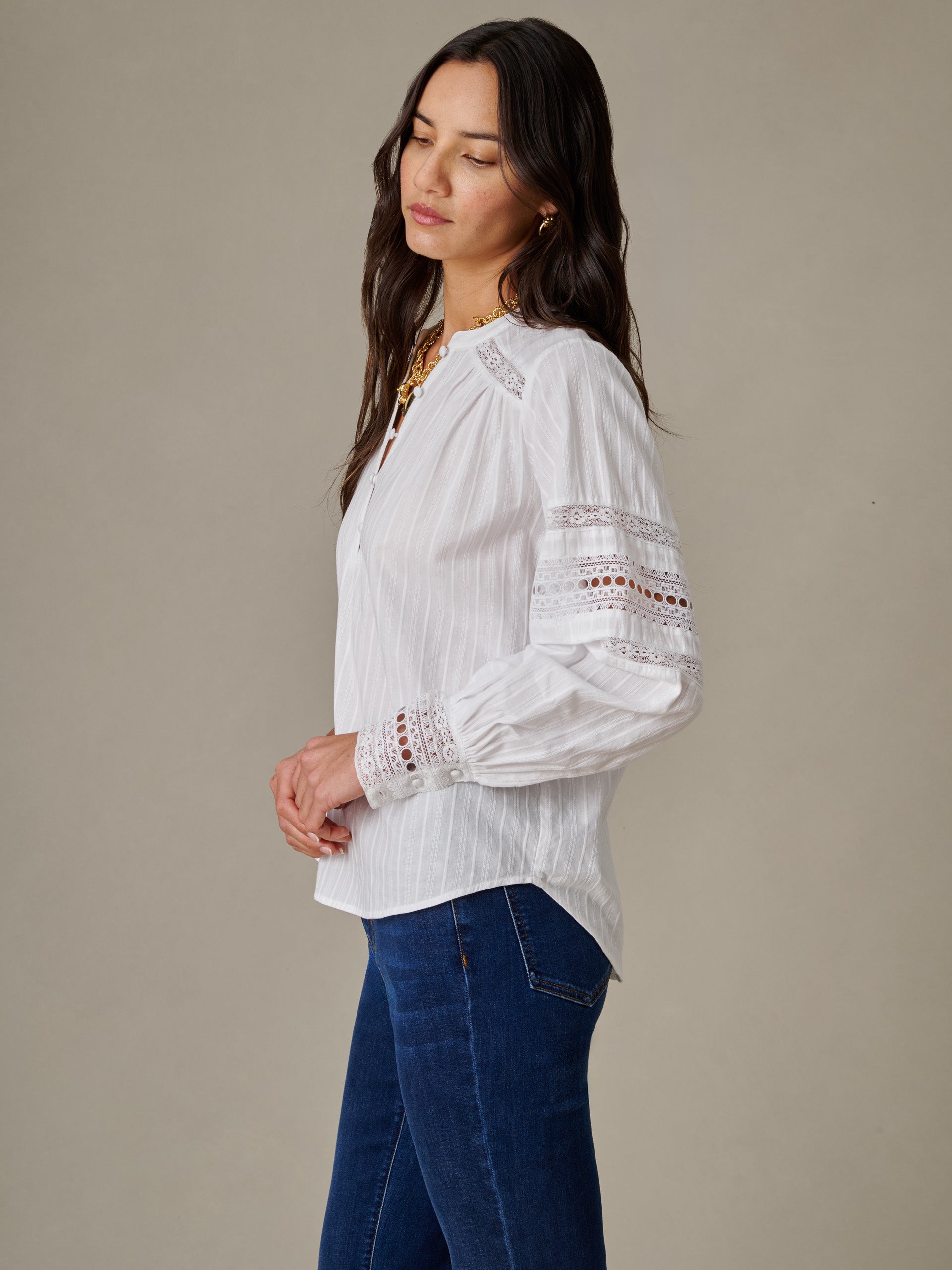Woman wearing a white Posey Blouse by J.McLaughlin with delicate lace details on sleeves, styled with blue jeans, showcasing timeless, effortlessly stylish fashion.