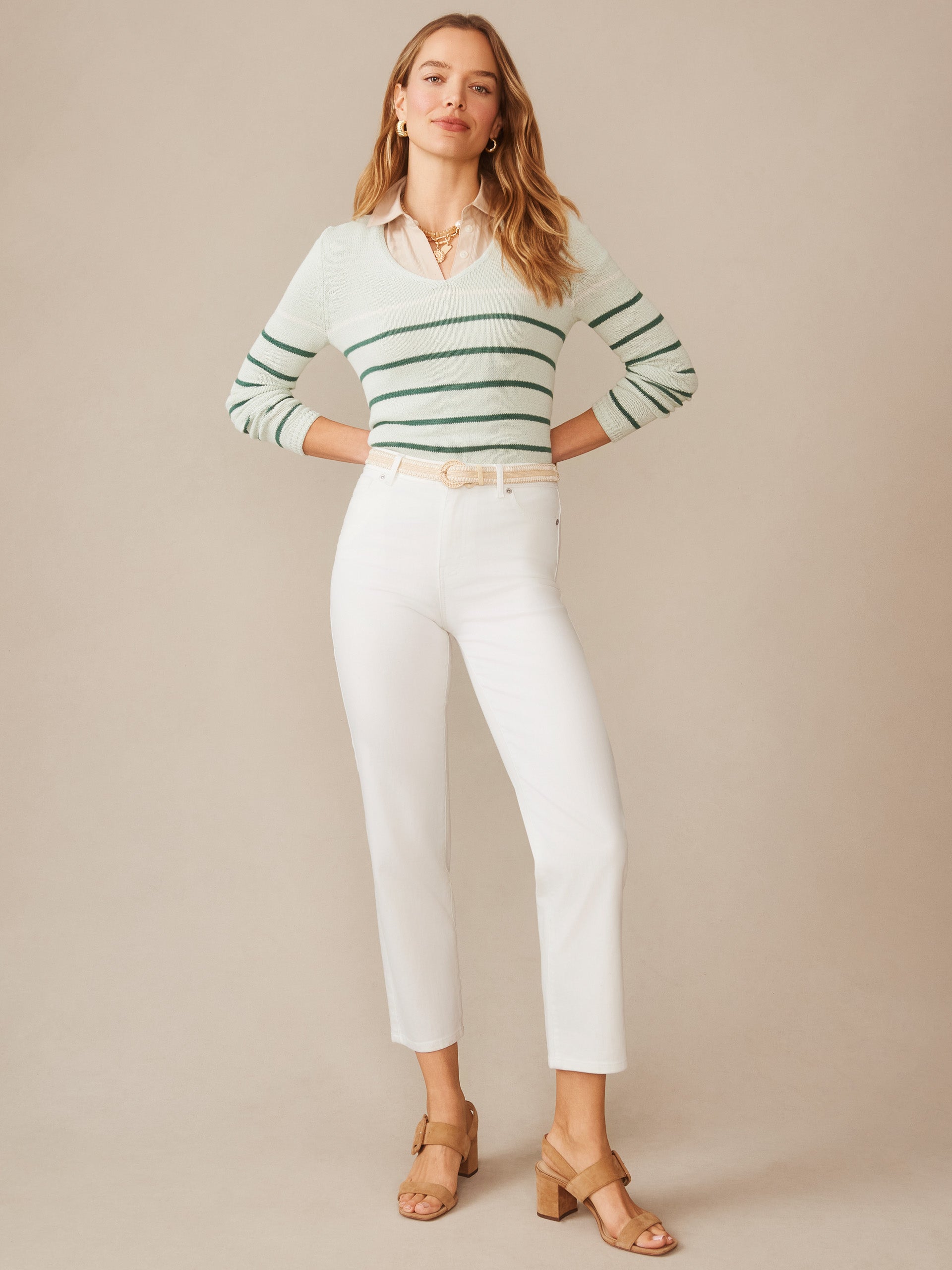 Woman models Ramona Linen Blend Sweater in Stripe by J.McLaughlin, featuring green stripes and a V-neck, styled with white pants and tan sandals, showcasing effortlessly stylish, enduring designs and innovative fabrics, a destination for defining style. Life, Well-Lived.