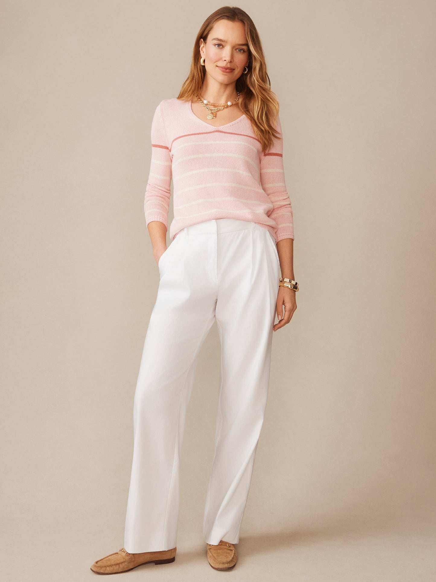 Woman wearing a pink and white striped Ramona Linen Blend Sweater in Stripe paired with white pants, showcasing J.McLaughlin’s effortlessly stylish, enduring designs.