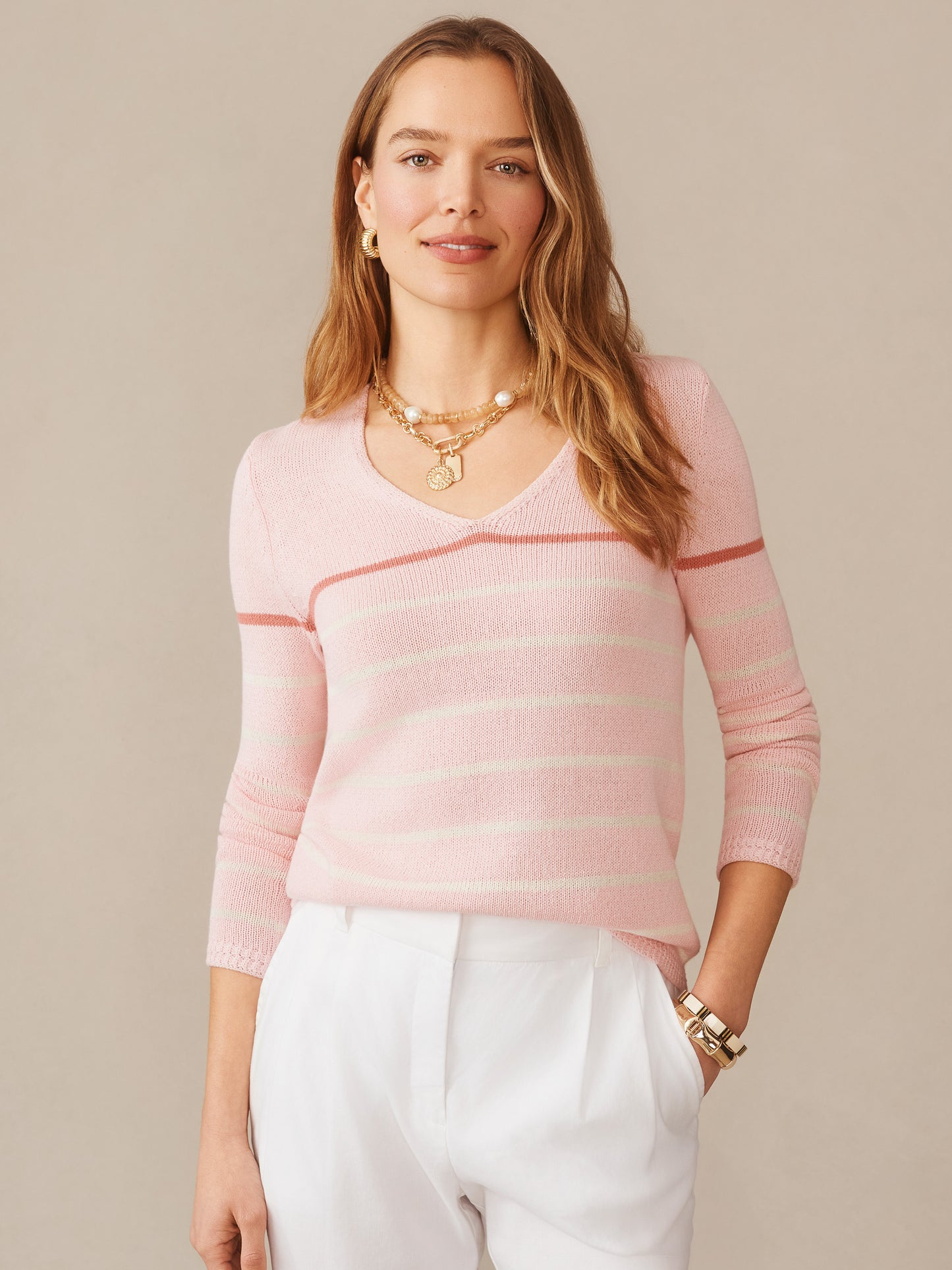 A woman wearing a Ramona Linen Blend Sweater in Stripe by J.McLaughlin in soft pink hues with white and darker pink stripes, paired with white pants, embodying effortlessly stylish, enduring designs with innovative fabrics in a legacy of timeless fashion. A destination for defining style. Life, Well-Lived.