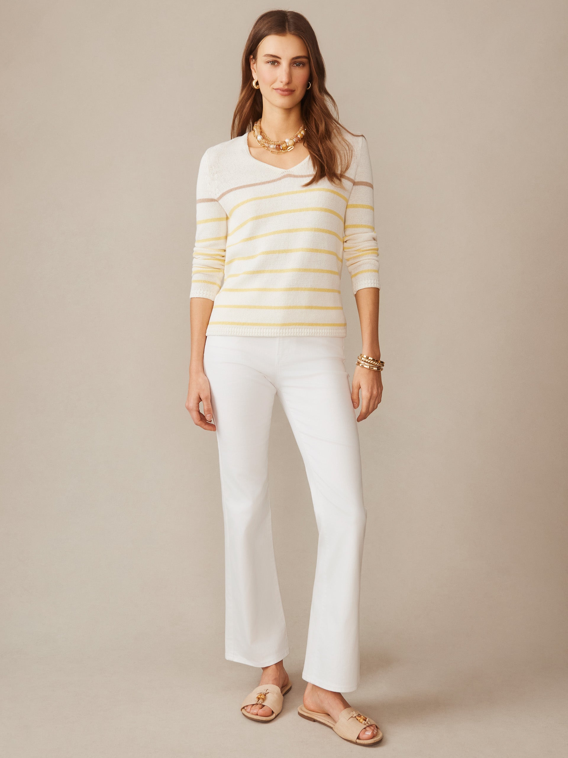 Woman wearing a Ramona Linen Blend Sweater in Stripe by J.McLaughlin, featuring soft yellow stripes and lightweight fabric, styled with white pants and gold accessories, embodying effortlessly stylish, enduring designs with a legacy of timeless fashion from a destination for defining style. Life, Well-Lived.