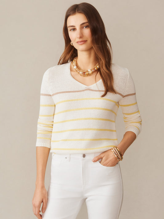 A woman wearing the Ramona Linen Blend Sweater in Stripe by J.McLaughlin featuring soft yellow and beige stripes, paired with white pants and layered necklaces, showcasing effortlessly stylish, enduring designs with innovative fabrics from a destination for defining style. Life, Well-Lived.