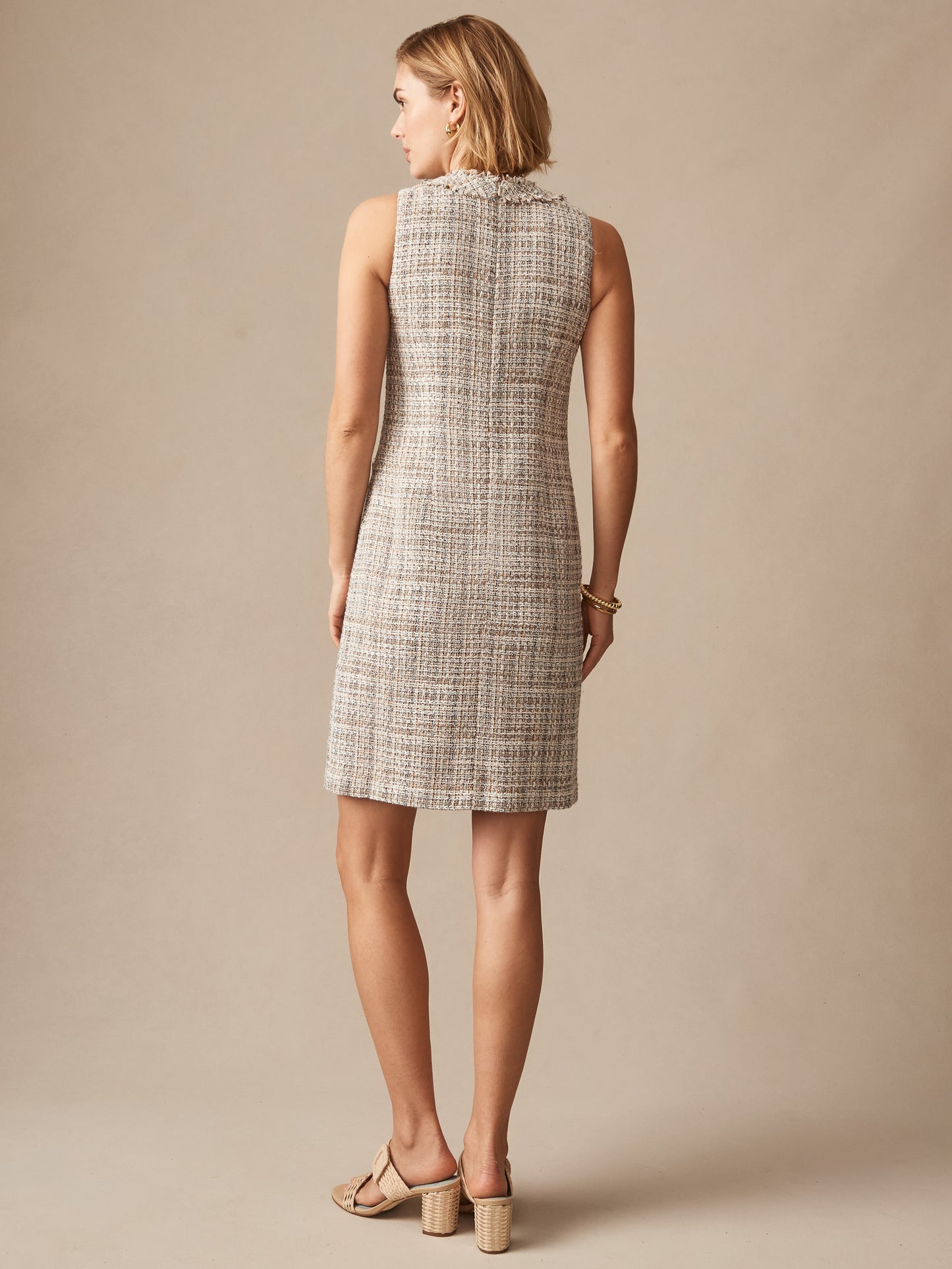 Back view of a woman wearing the Regina Tweed Dress by J.McLaughlin, featuring a taupe and off-white textured fabric, accessorized with bracelets and block-heeled sandals, showcasing effortlessly stylish, enduring designs and innovative fabrics for a legacy of timeless fashion. A destination for defining style. Life, Well-Lived.