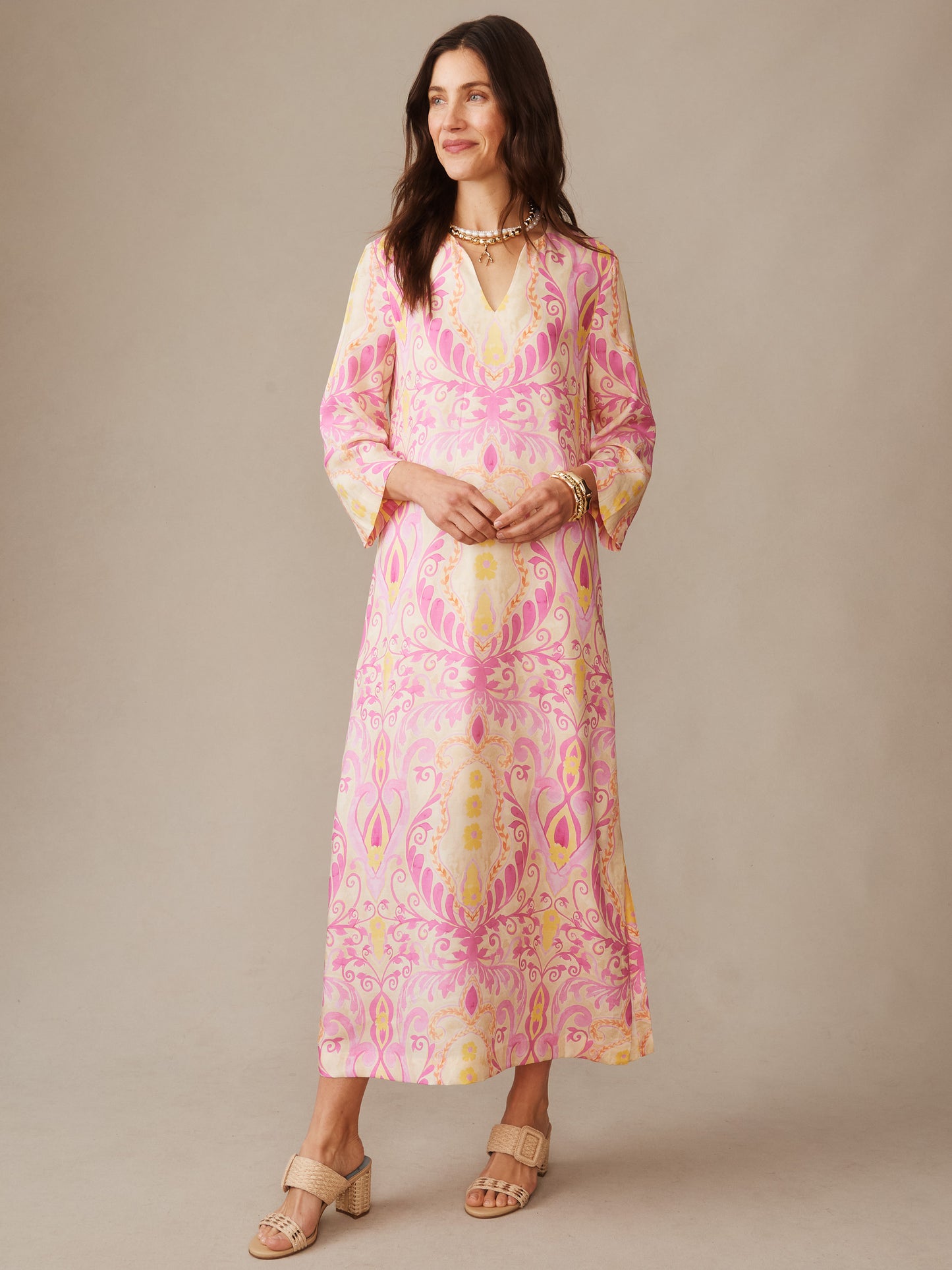 Woman wearing a Roni Silk Blend Dress in Midi Deco Bloom by J.McLaughlin featuring a pink and yellow intricate floral pattern, styled with sandals and jewelry, embodying effortlessly stylish and enduring designs.