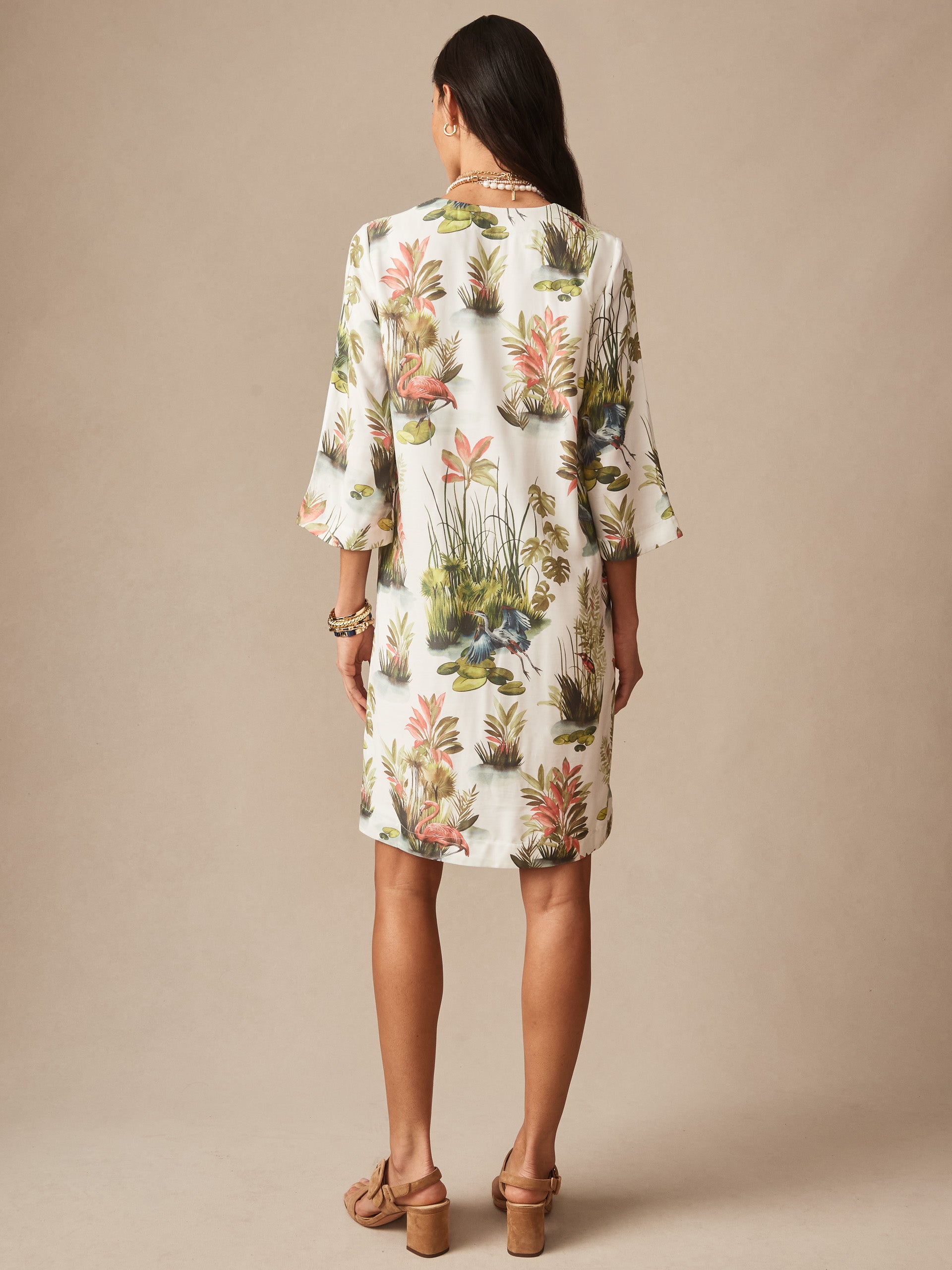 Woman wearing the Roni Dress in Tidal Palms by J.McLaughlin, featuring a white background with coral and green botanical prints, showcasing effortlessly stylish, enduring designs and innovative fabrics.
