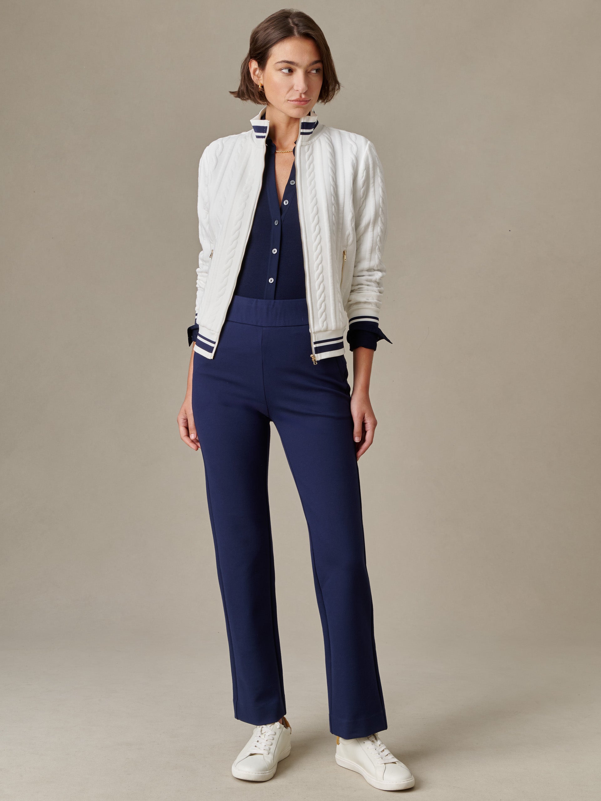 Woman wearing navy Rory Pants by J.McLaughlin paired with a navy button-up shirt, white textured jacket, and white sneakers, showcasing timeless style and craftsmanship.