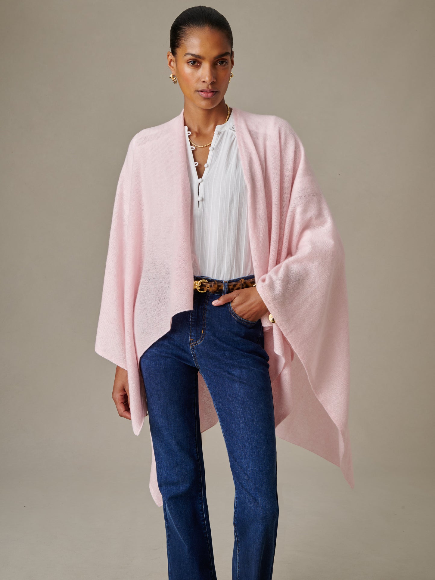 Woman wearing a soft pink Rossi Cashmere Wrap by J.McLaughlin over a white blouse and blue jeans, showcasing effortlessly stylish and enduring design for timeless fashion.