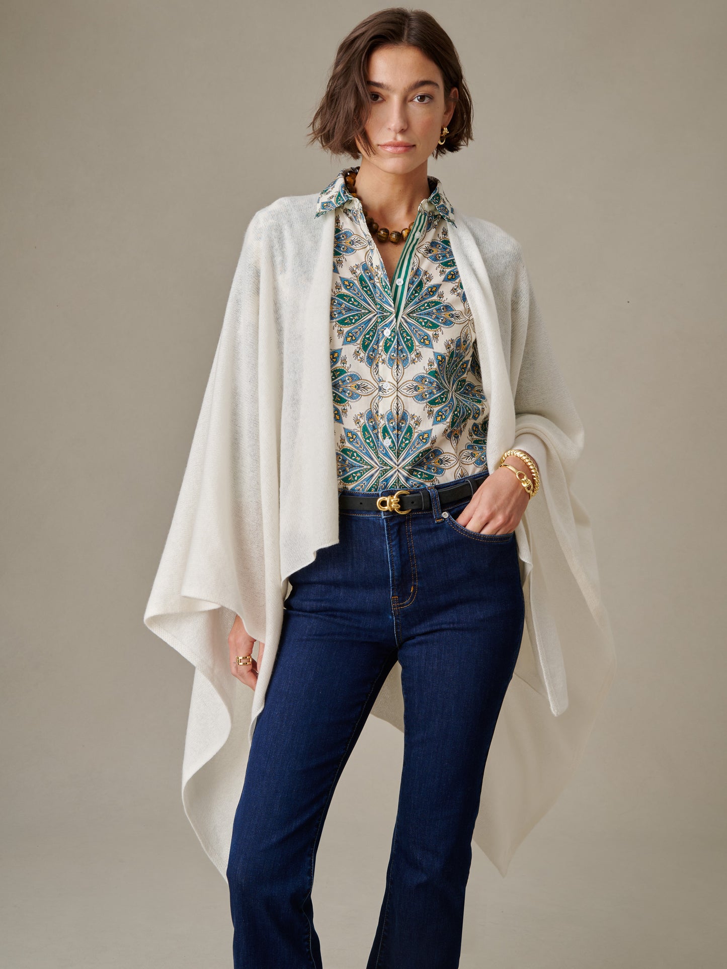 Woman wearing a white Rossi Cashmere Wrap over a patterned blouse with blue and green floral design, paired with dark blue jeans and gold jewelry, styled by J.McLaughlin.