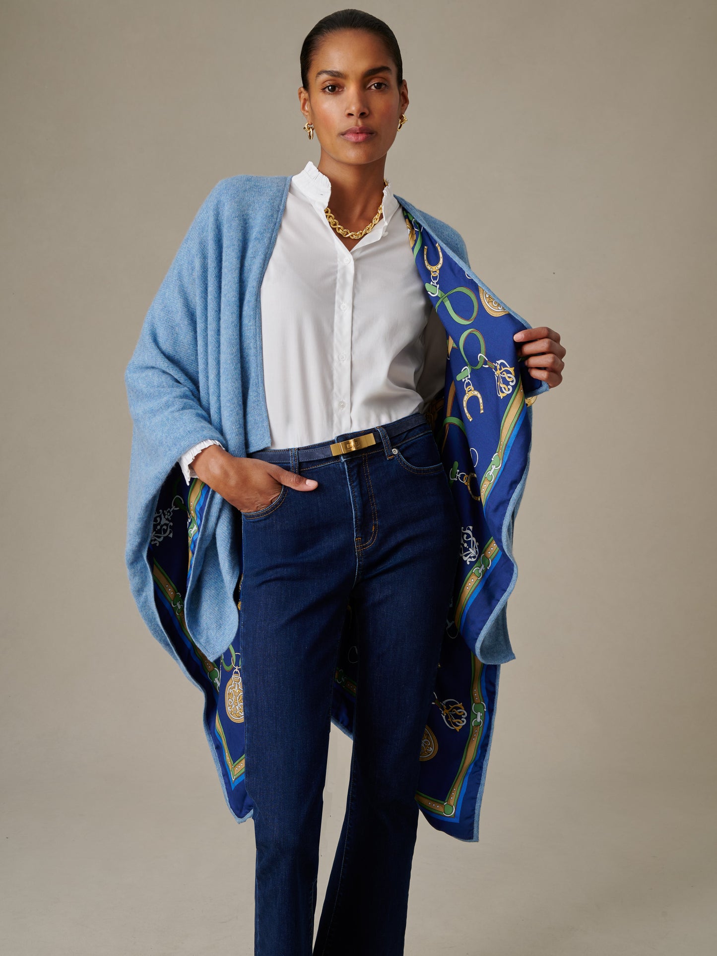 Woman wearing a white blouse and dark jeans with a light blue Rossi Cashmere Wrap in Fairfax Crest featuring a patterned blue and green lining, styled by J.McLaughlin.