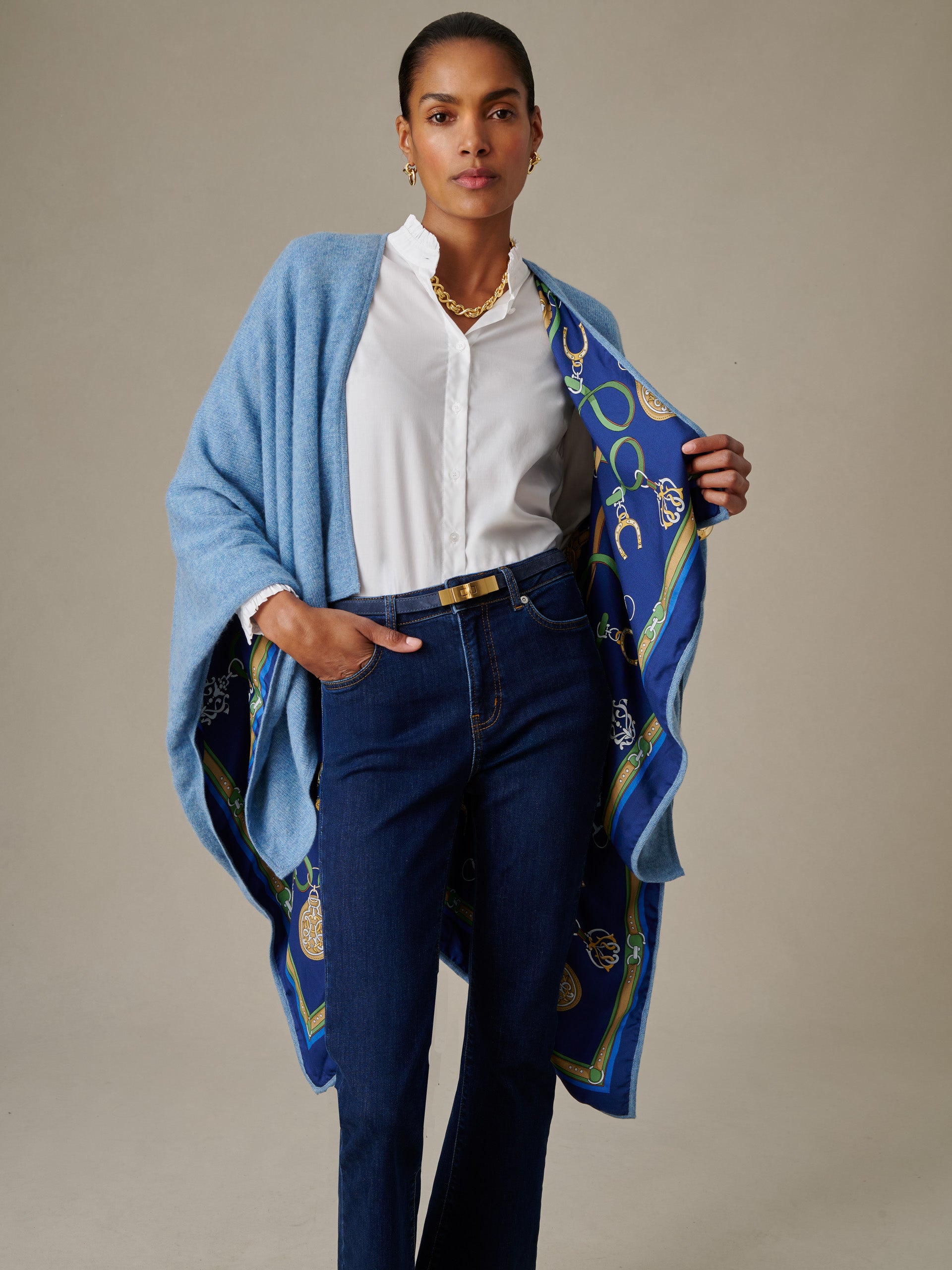 Woman wearing a white blouse and dark jeans with a light blue Rossi Cashmere Wrap in Fairfax Crest featuring a patterned blue and green lining, styled by J.McLaughlin.