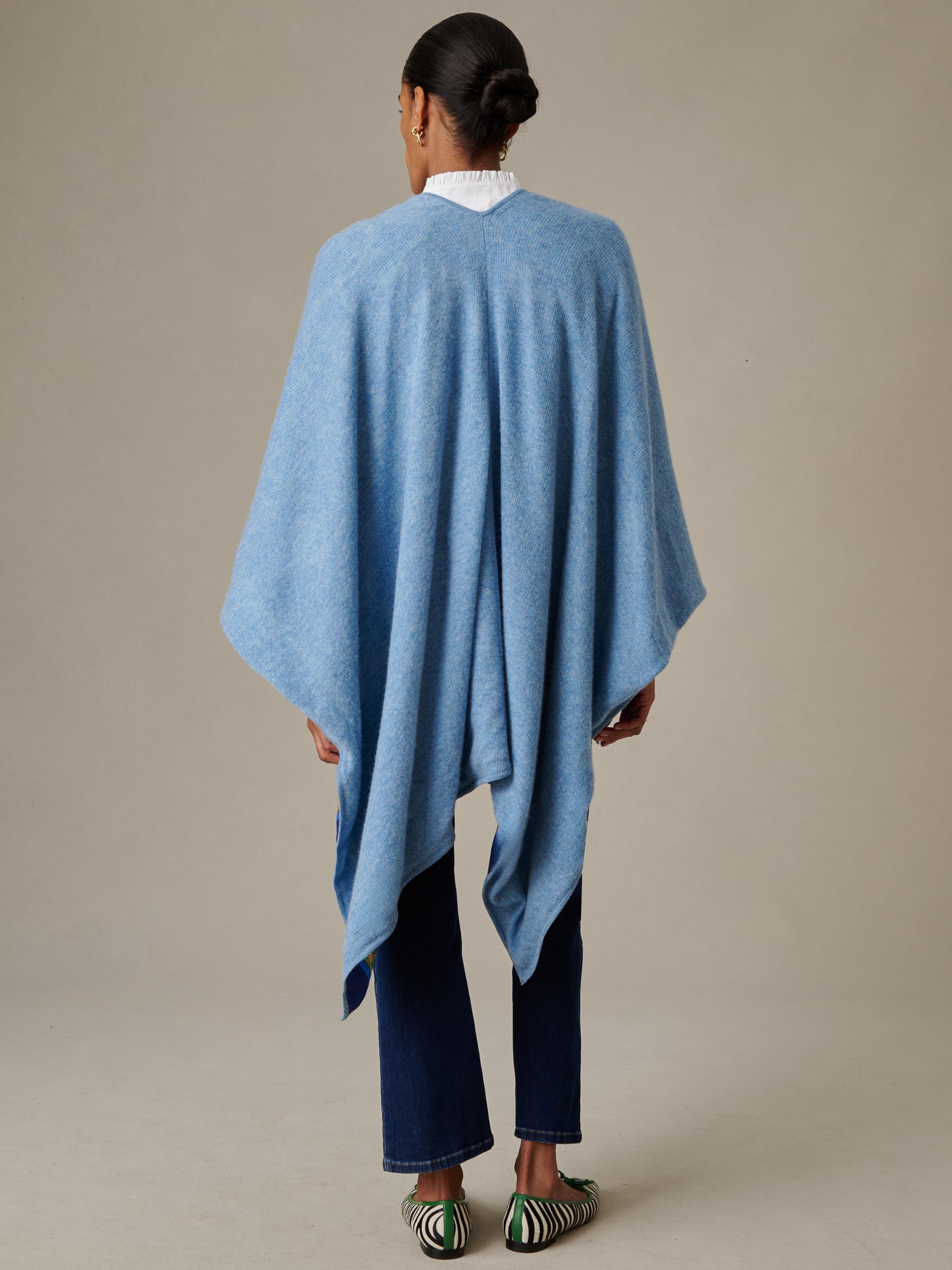 Woman seen from behind wearing a soft blue Rossi Cashmere Wrap in Fairfax Crest by J.McLaughlin over dark jeans and striped shoes, showcasing elegant and enduring style.