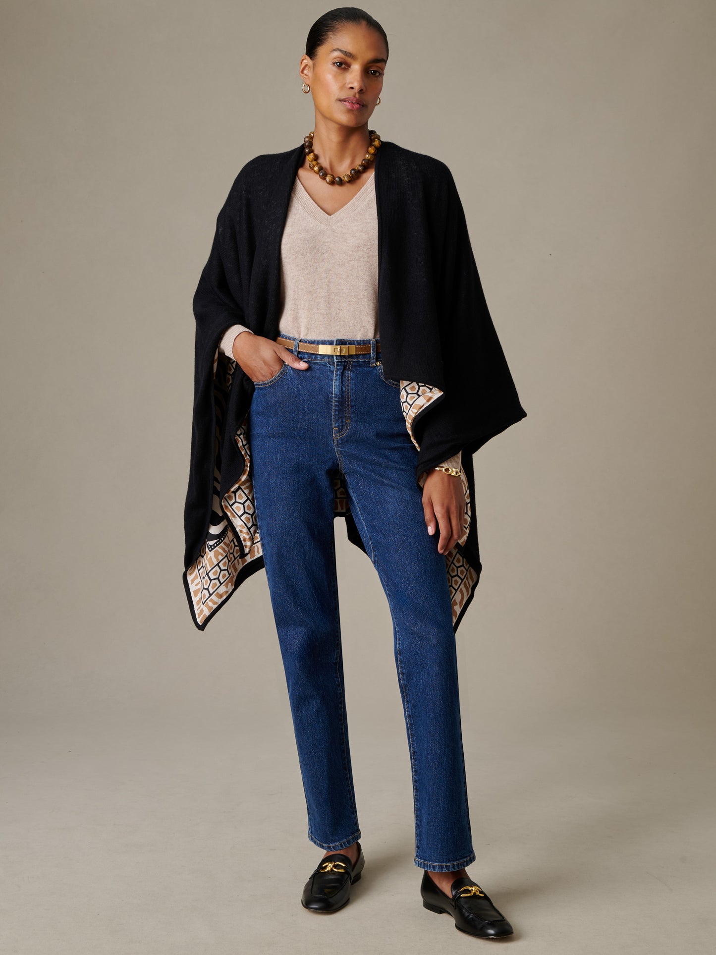 Woman wearing a Rossi Cashmere Wrap in Wild Medley Border by J.McLaughlin, styled over a beige v-neck top and blue jeans, showcasing a timeless, effortlessly stylish look.