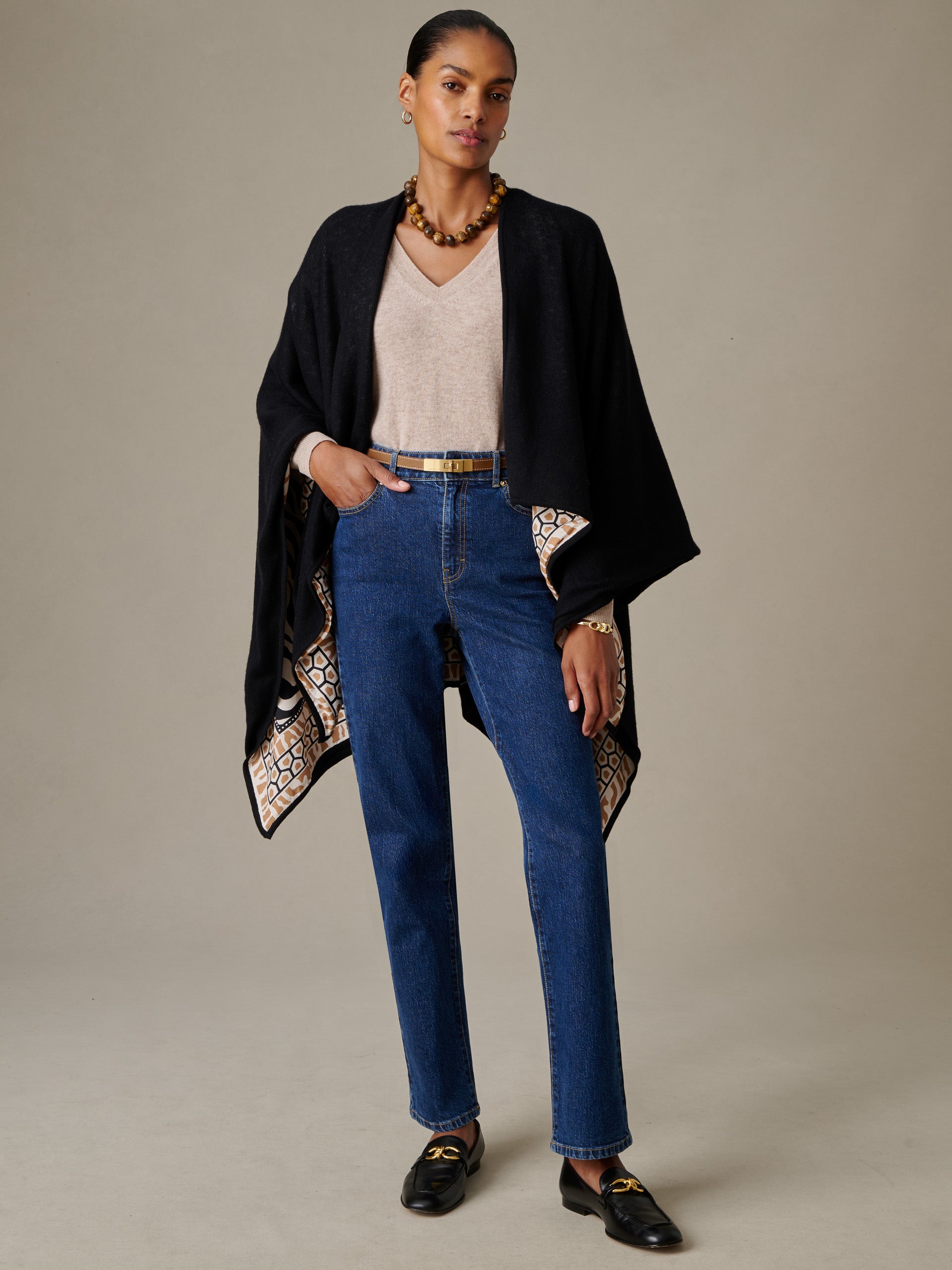 Woman wearing a Rossi Cashmere Wrap in Wild Medley Border by J.McLaughlin, styled over a beige v-neck top and blue jeans, showcasing a timeless, effortlessly stylish look.