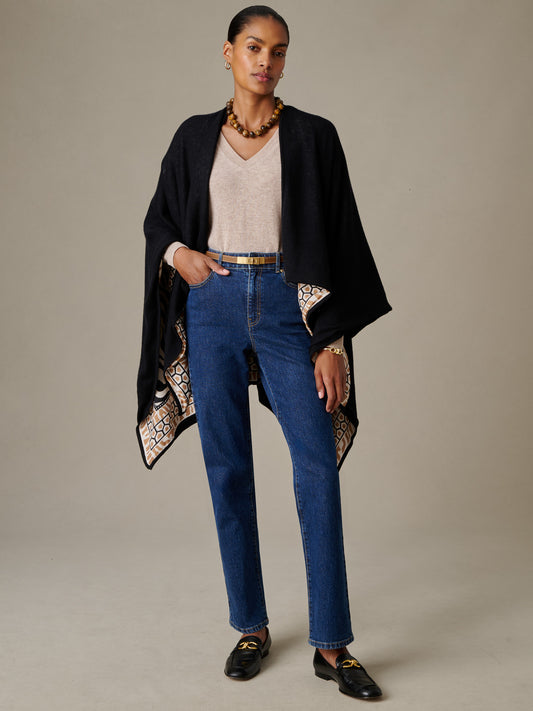 Woman wearing a Rossi Cashmere Wrap in Wild Medley Border by J.McLaughlin, styled over a beige v-neck top and blue jeans, showcasing a timeless, effortlessly stylish look.