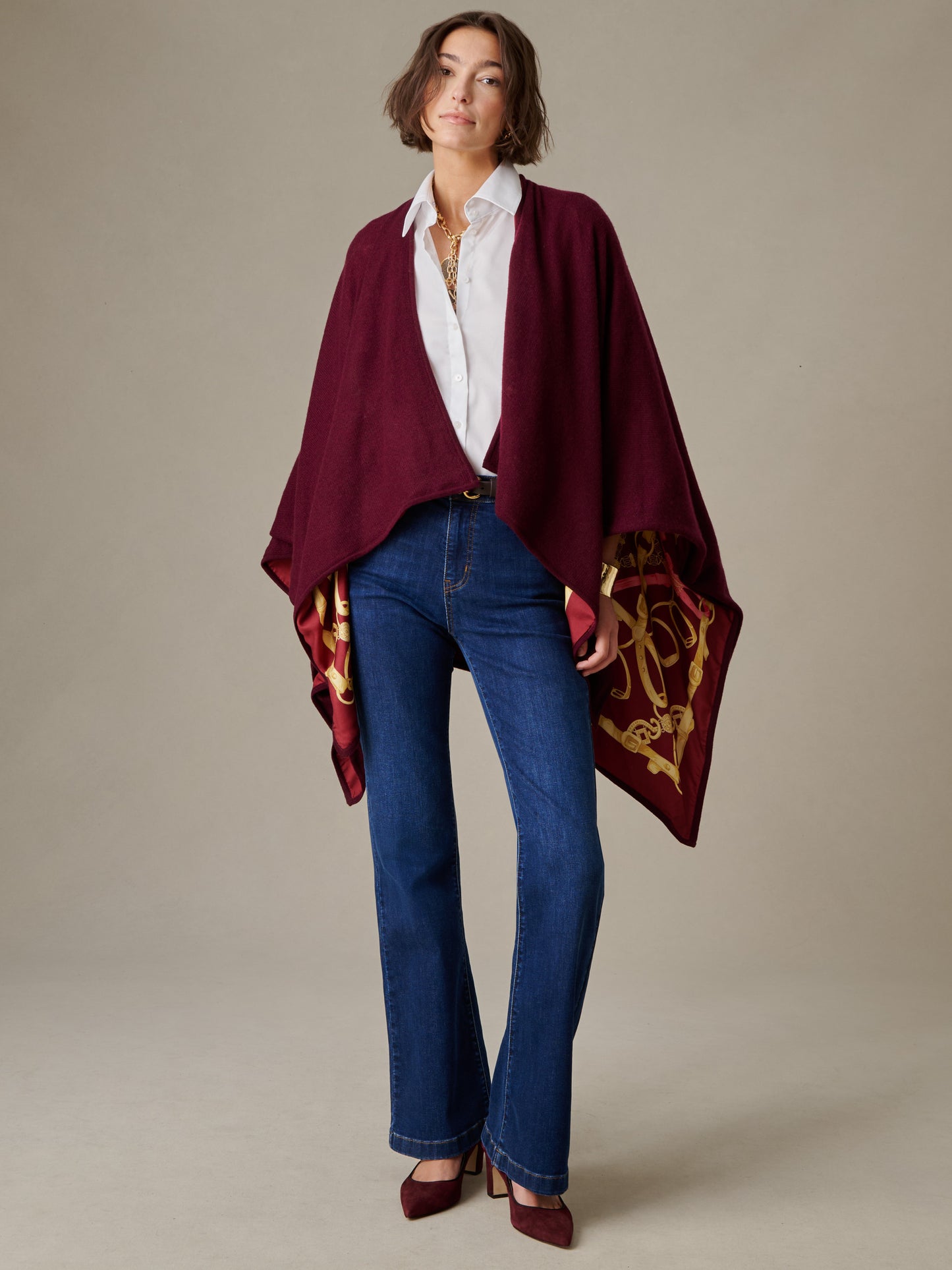 Woman modeling Rossi Cashmere Wrap in Grand Heraldic Border by J.McLaughlin paired with blue jeans, white blouse, and burgundy heels, showcasing timeless style and elegant layering.