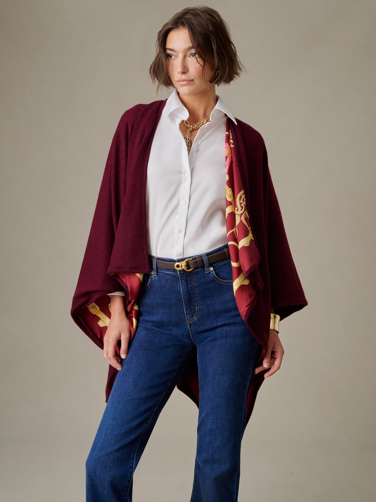 Woman wearing a white shirt and jeans with a burgundy Rossi Cashmere Wrap in Grand Heraldic Border featuring a gold heraldic design by J.McLaughlin, styled with a black belt and layered jewelry.