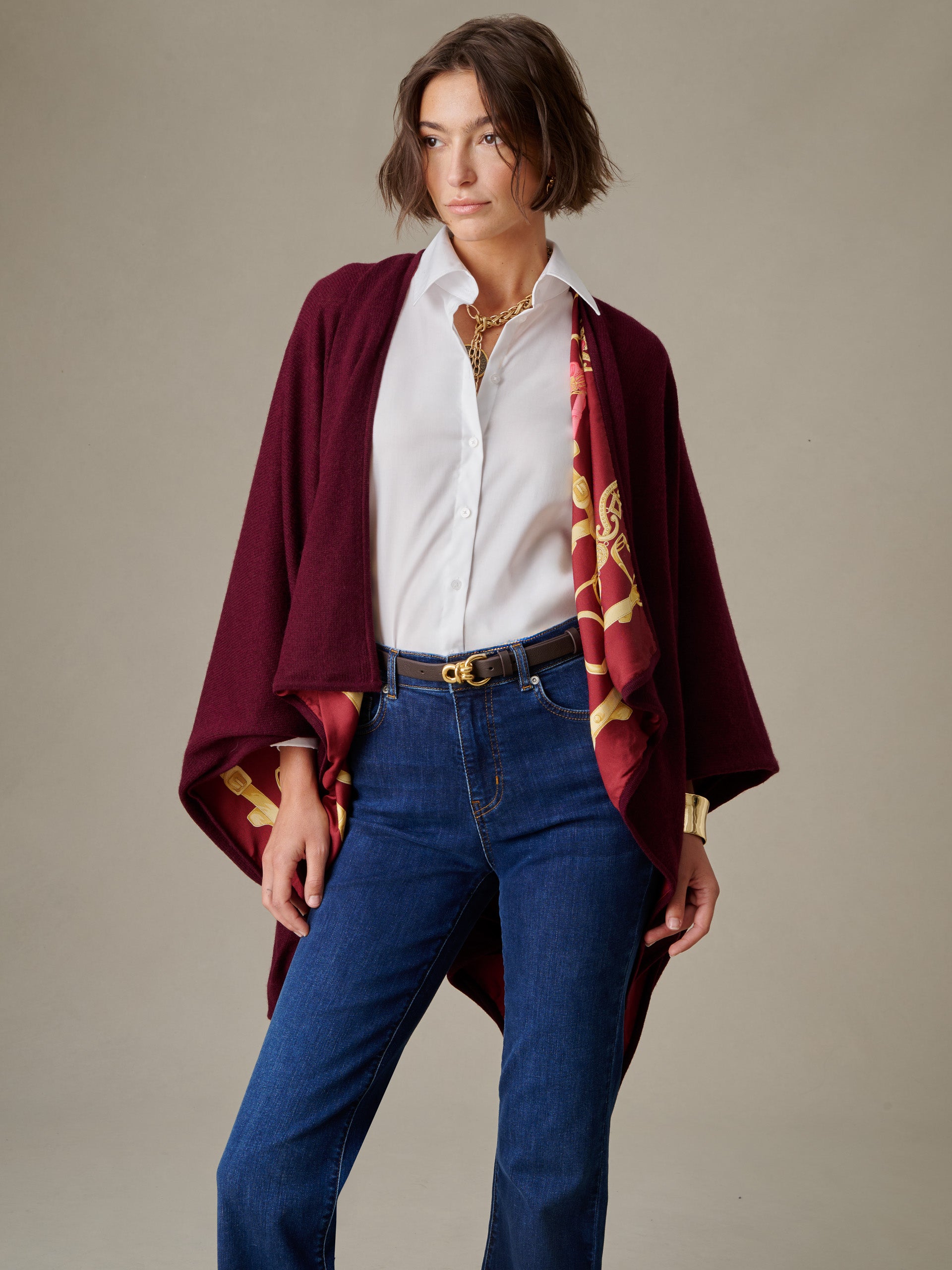 Woman wearing a white shirt and jeans with a burgundy Rossi Cashmere Wrap in Grand Heraldic Border featuring a gold heraldic design by J.McLaughlin, styled with a black belt and layered jewelry.