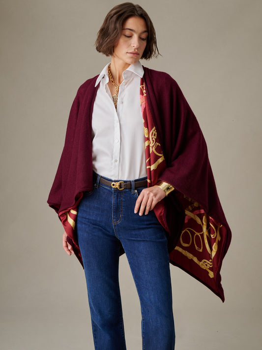 Woman wearing a white shirt and blue jeans draped in a Rossi Cashmere Wrap in Grand Heraldic Border by J.McLaughlin, showcasing timeless style with rich burgundy and gold detailing.