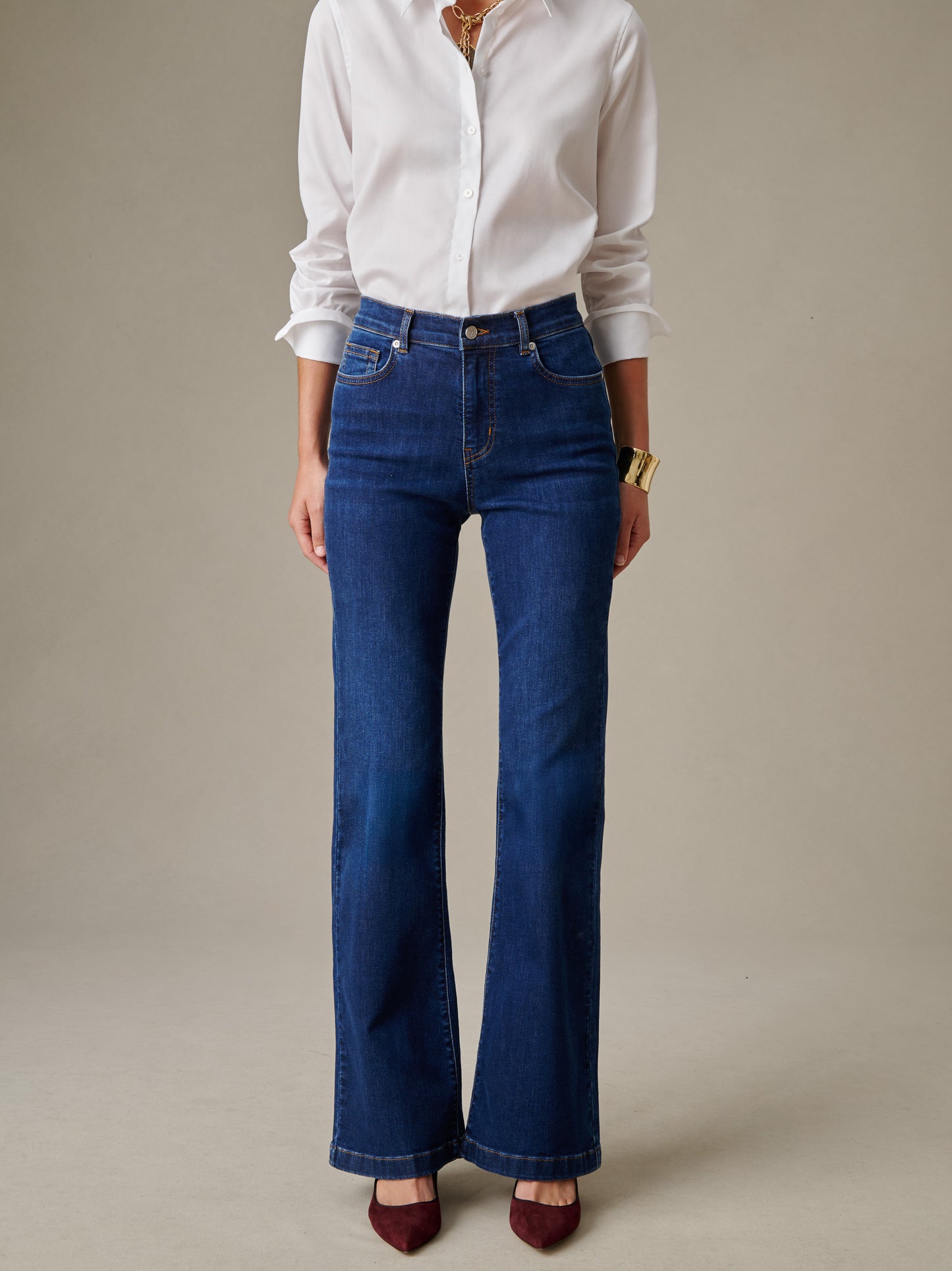 A woman modeling Domino Jeans by J.McLaughlin, wearing a crisp white button-up shirt and gold accessories, showcasing a timeless and stylish denim design.