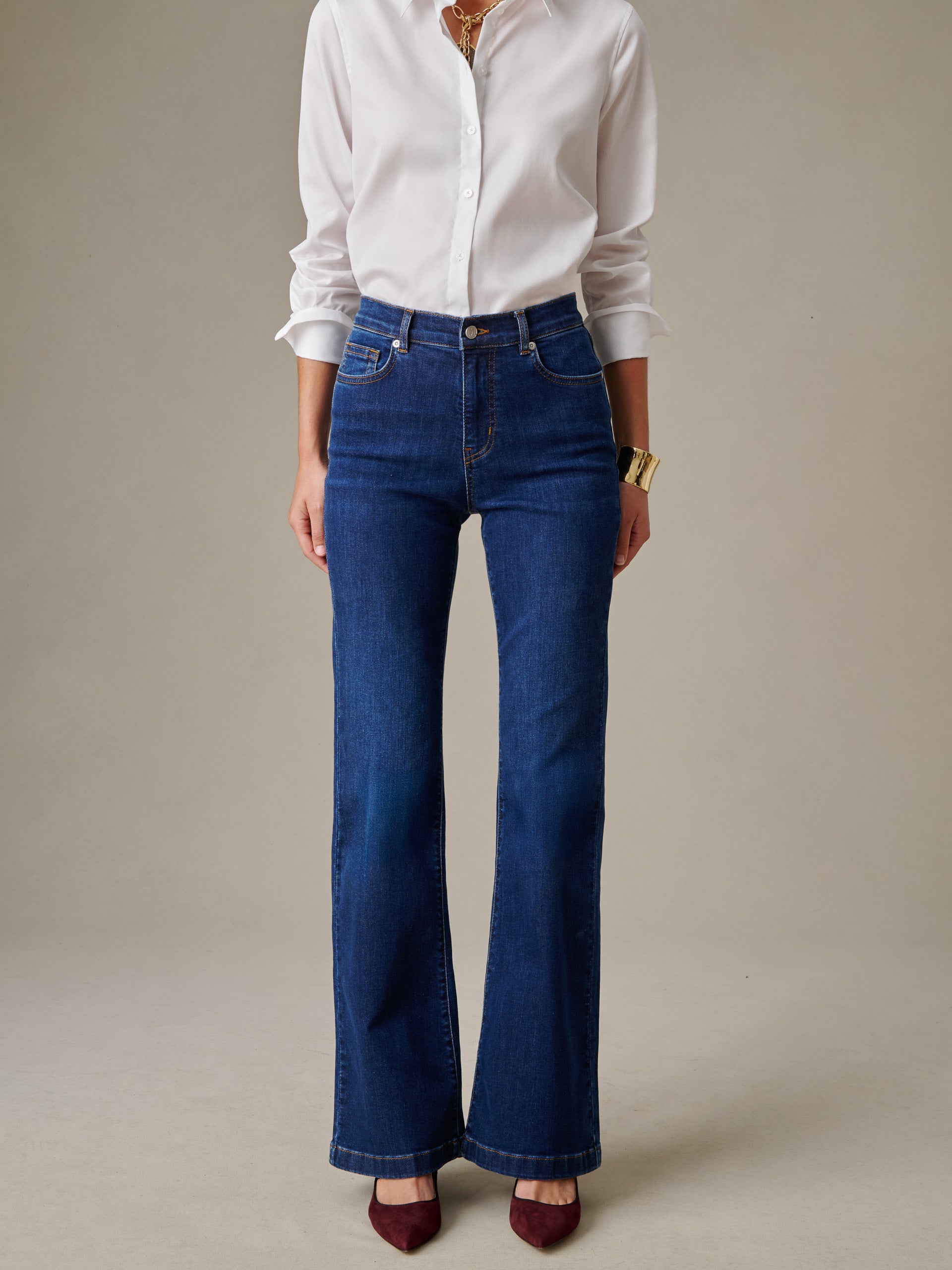 A woman modeling Domino Jeans by J.McLaughlin, wearing a crisp white button-up shirt and gold accessories, showcasing a timeless and stylish denim design.