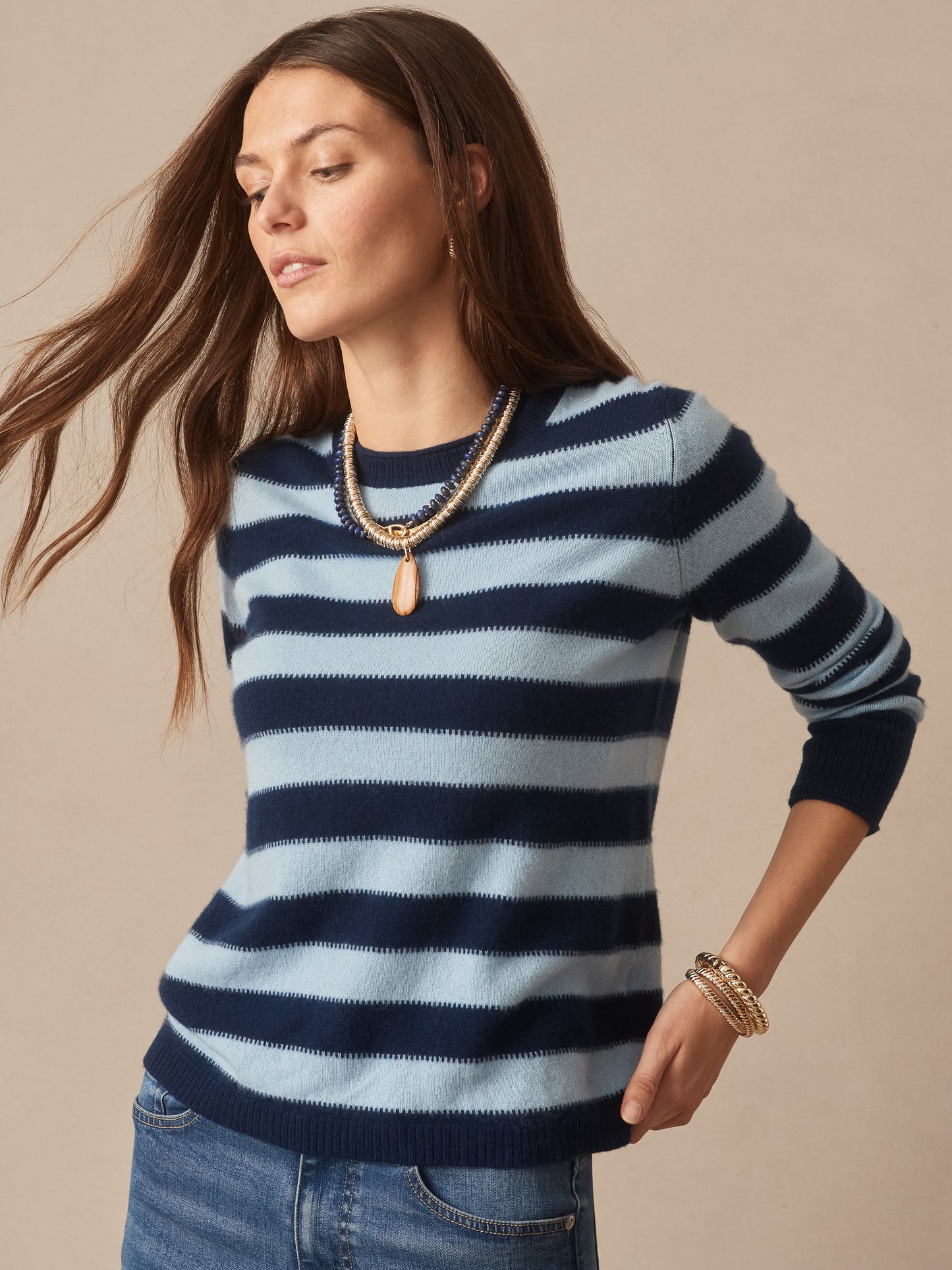Woman wearing a Ruby Cashmere Sweater in Stripe by J.McLaughlin, featuring navy and light blue stripes, styled with gold jewelry and denim jeans, embodying effortlessly stylish, enduring designs with a legacy of timeless fashion. A destination for defining style. Life, Well-Lived.