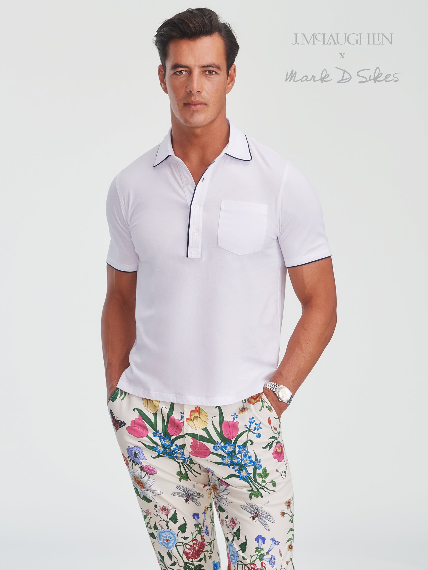 Male model wearing a crisp white Ryan Polo with navy trim and floral patterned pants by J.McLaughlin, showcasing effortlessly stylish, enduring designs and innovative fabrics in a legacy of timeless fashion. A destination for defining style. Life, Well-Lived.