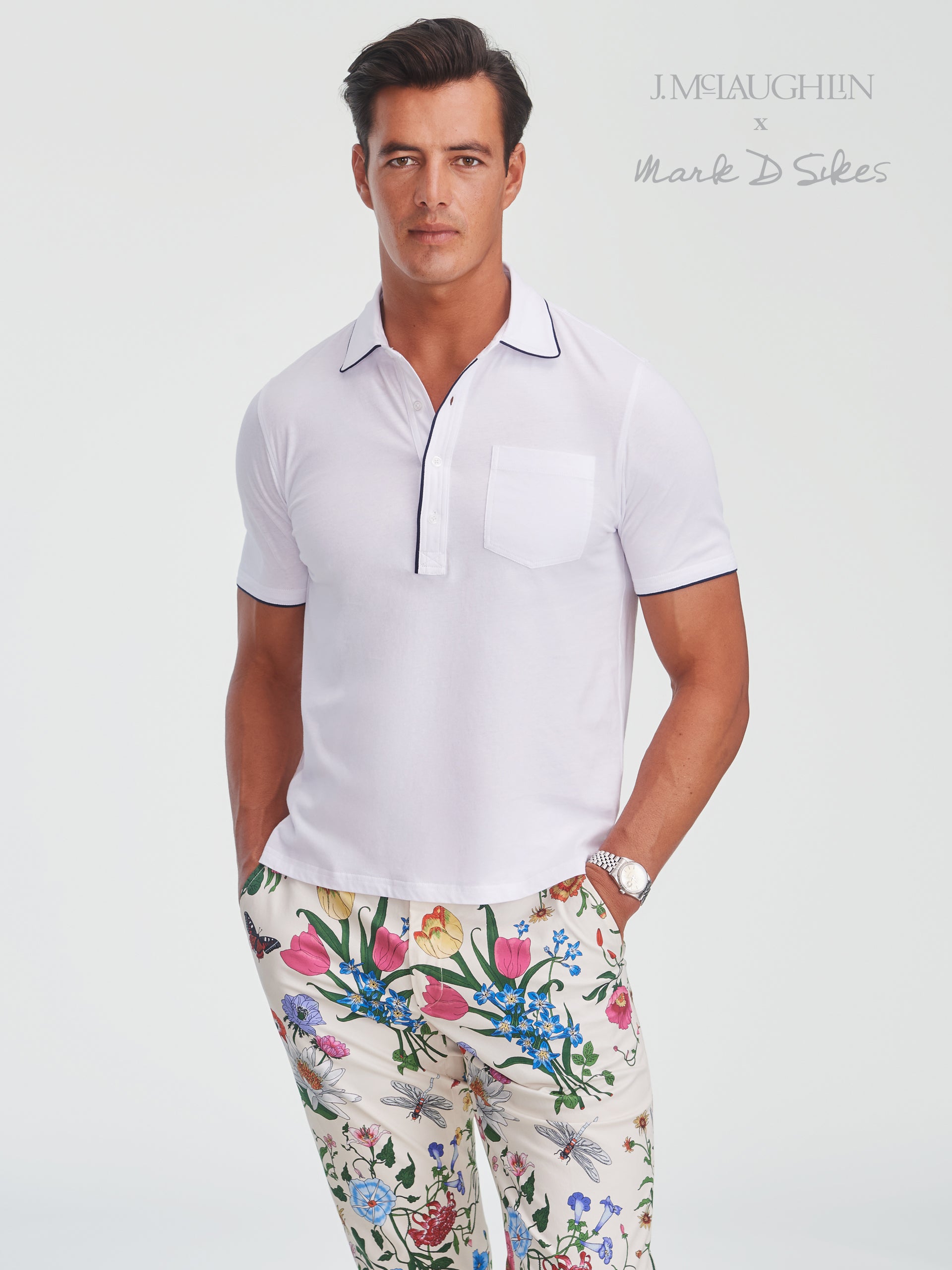 Male model wearing a crisp white Ryan Polo with navy trim and floral patterned pants by J.McLaughlin, showcasing effortlessly stylish, enduring designs and innovative fabrics in a legacy of timeless fashion. A destination for defining style. Life, Well-Lived.
