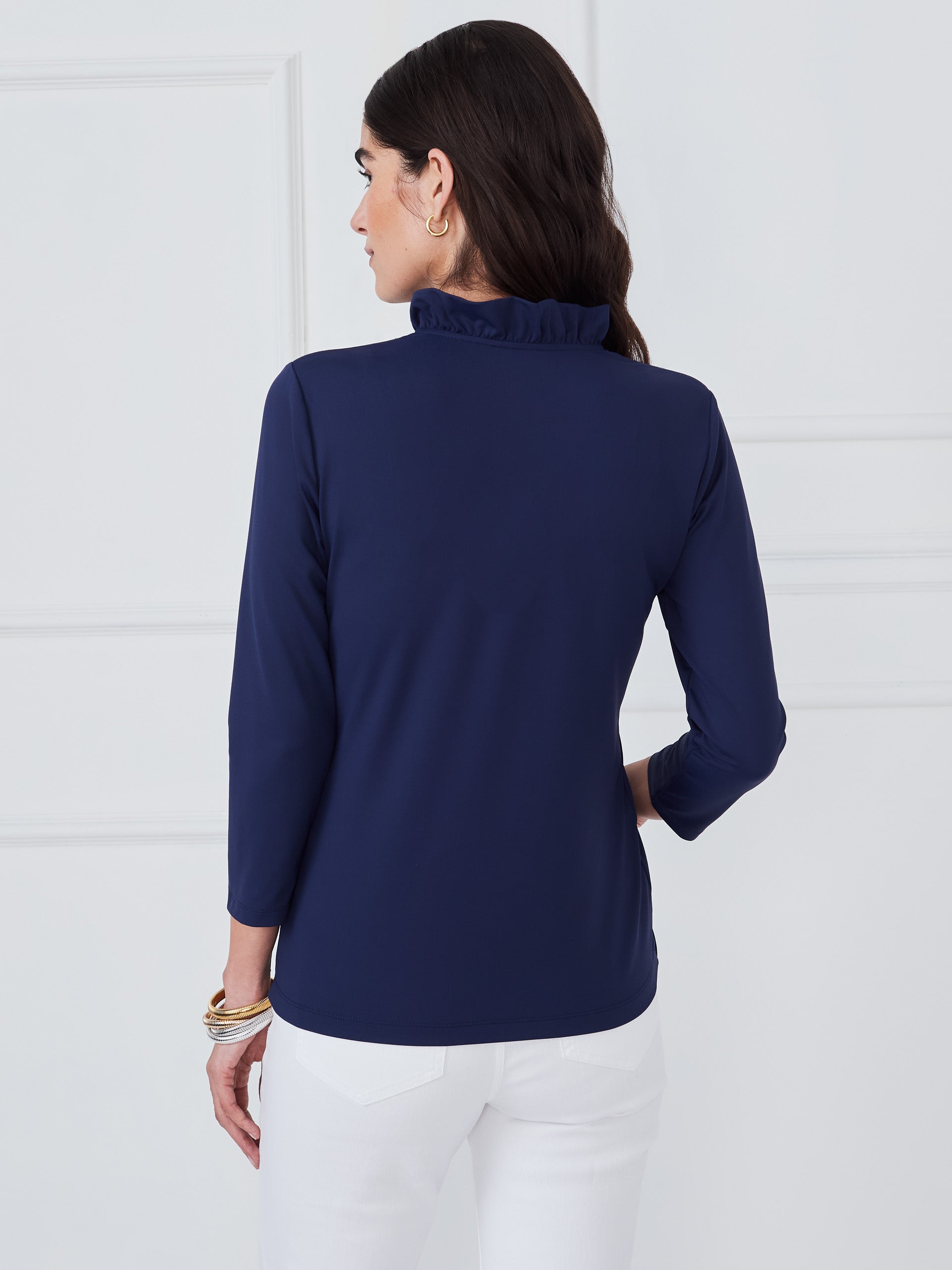 Woman wearing a navy Kate Ruffle Top by J.McLaughlin, showcasing effortless style with a ruffled neckline and long sleeves, embodying enduring designs and a legacy of timeless fashion. A destination for defining style. Life, Well-Lived.