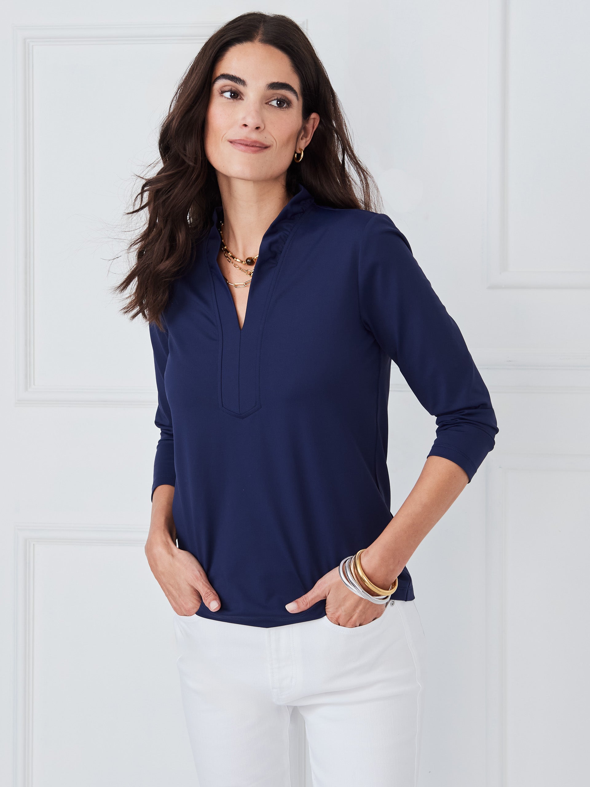 A woman wears a navy Kate Ruffle Top by J.McLaughlin paired with white pants, showcasing effortlessly stylish design and enduring quality for a refined, timeless look.