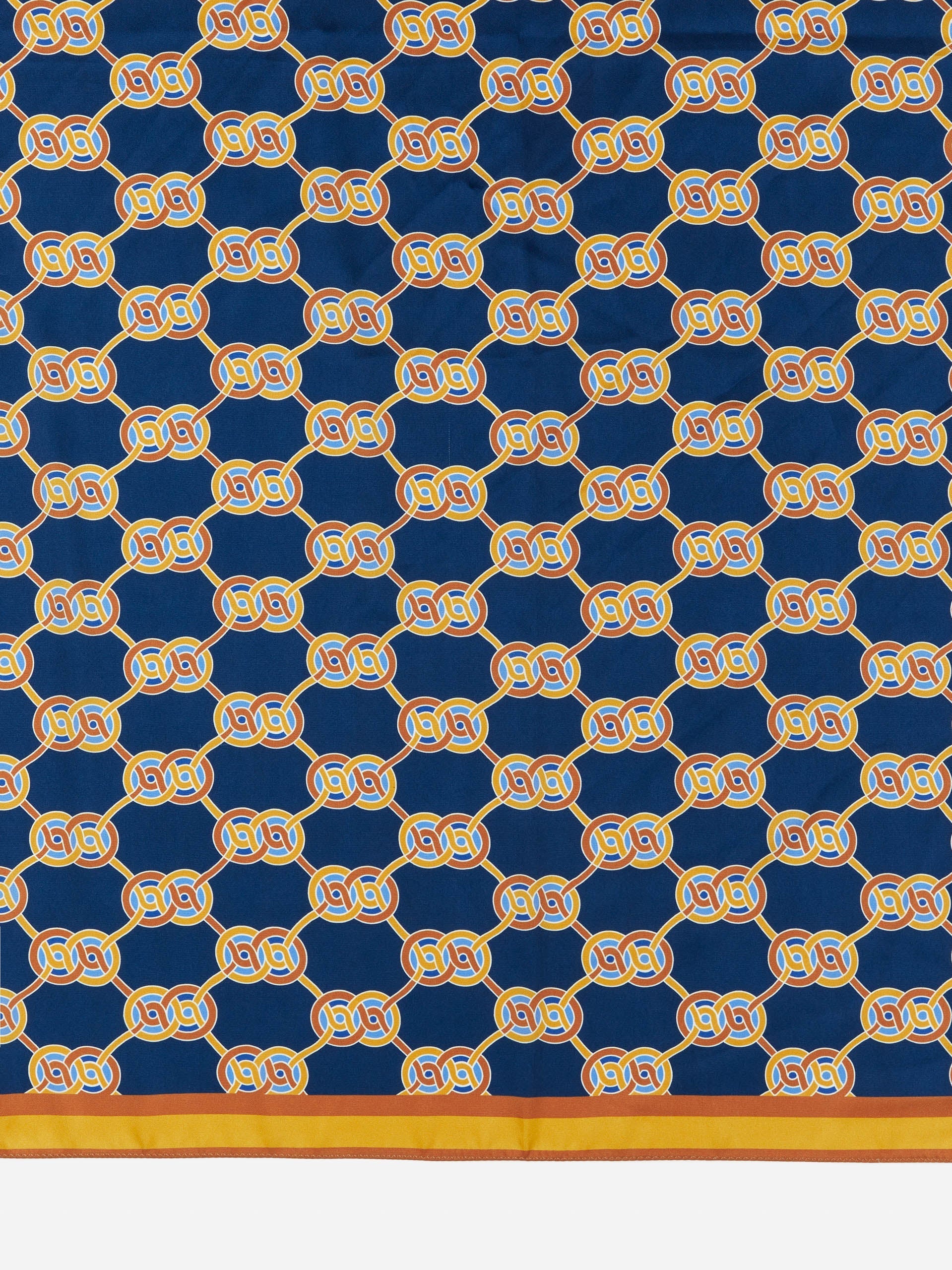 Gemma Scarf in Heraldic Knot by J.McLaughlin features a navy background with an intricate gold knot pattern, reflecting effortlessly stylish, enduring designs and innovative fabrics. A destination for defining style. Life, Well-Lived.