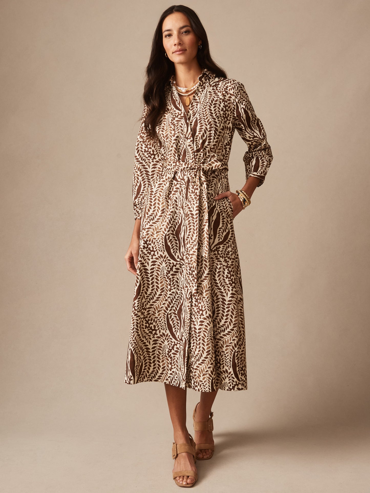 Woman wearing the Sena Dress in Coral Current by J.McLaughlin, featuring an elegant botanical print and belted waist, paired with stylish sandals and accessories, embodying effortlessly stylish, enduring designs, and innovative fabrics for a destination for defining style. Life, Well-Lived.