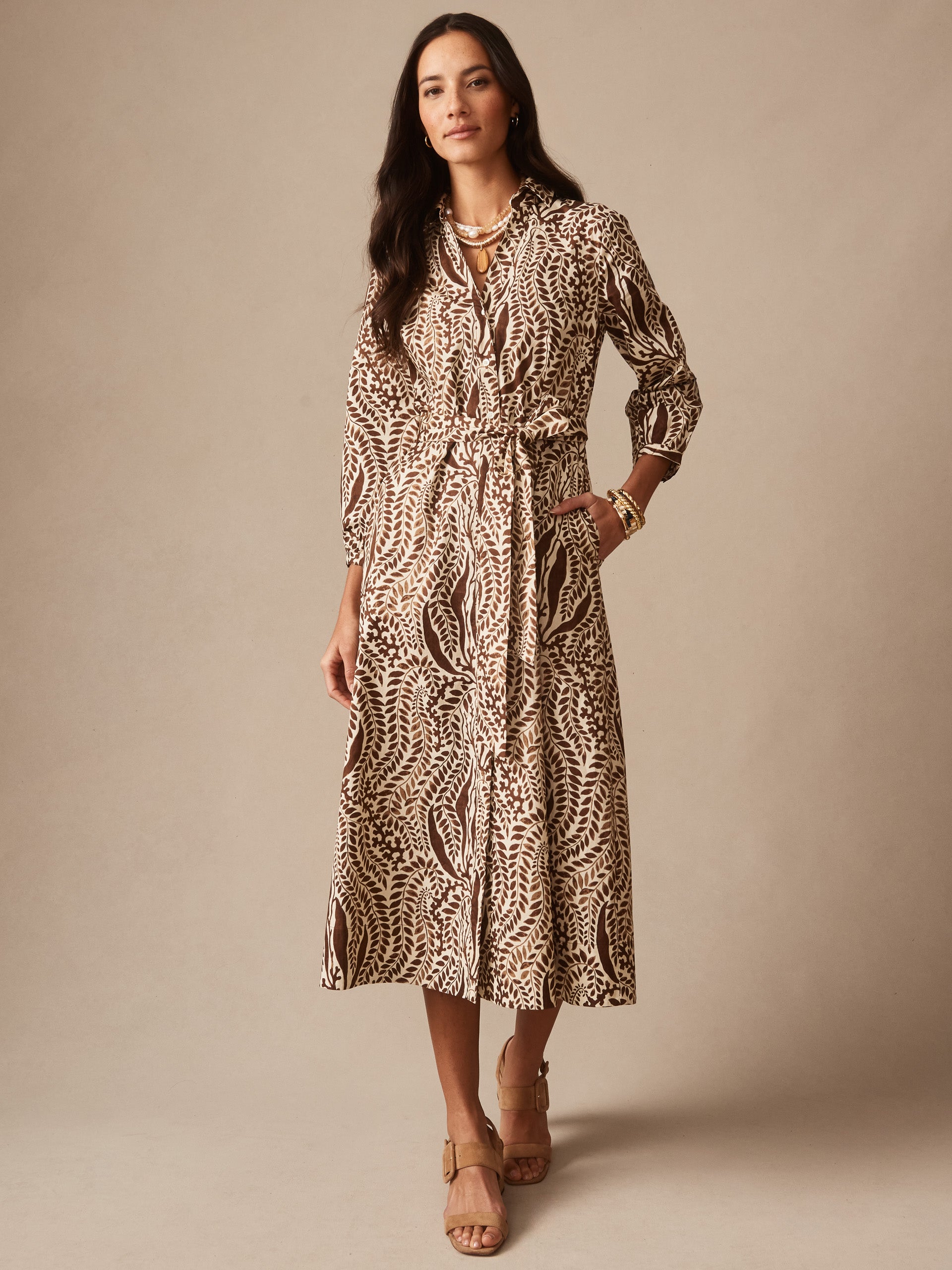 Woman wearing the Sena Dress in Coral Current by J.McLaughlin, featuring an elegant botanical print and belted waist, paired with stylish sandals and accessories, embodying effortlessly stylish, enduring designs, and innovative fabrics for a destination for defining style. Life, Well-Lived.
