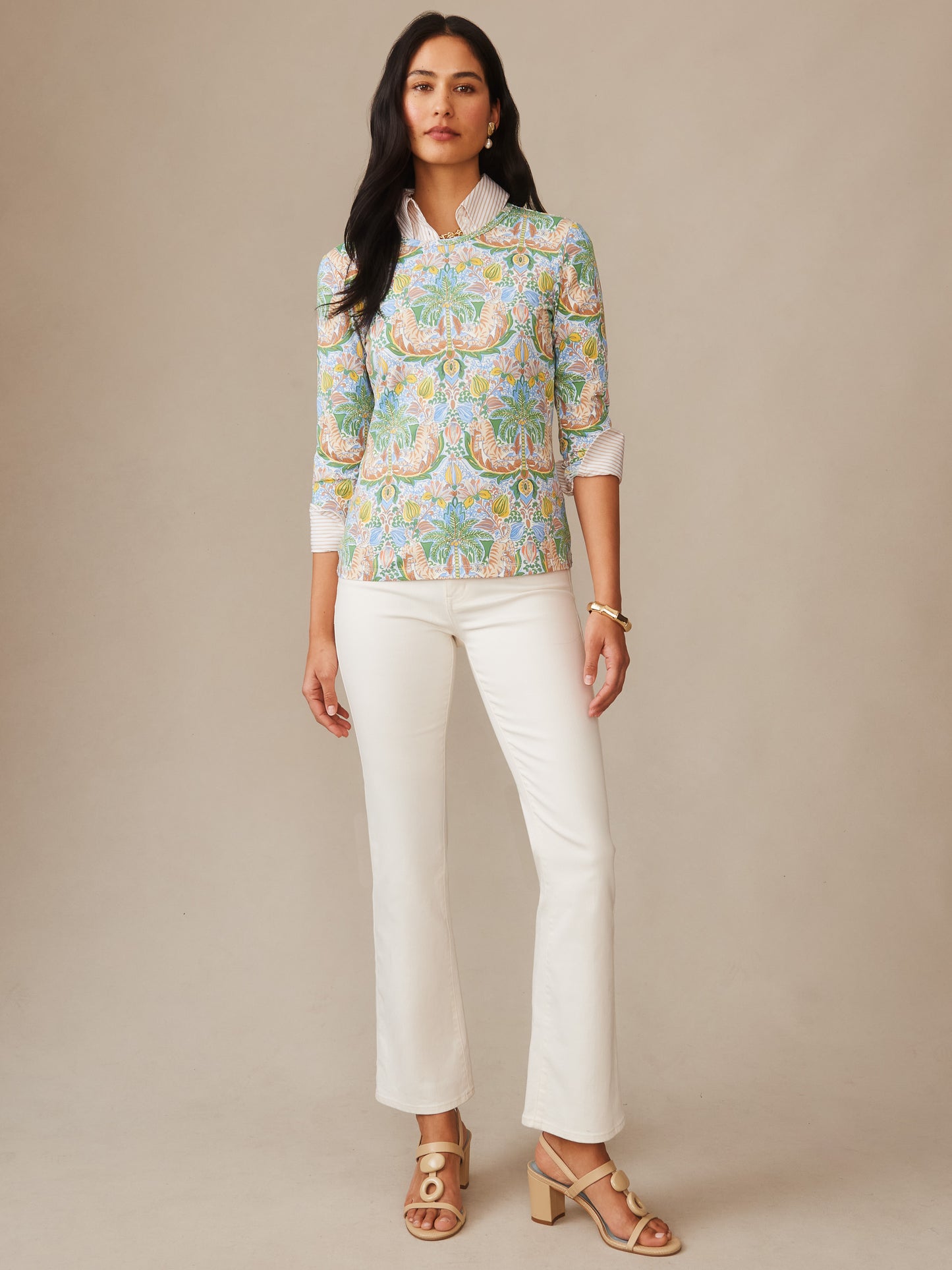 Woman modeling the Signature Tee in Tigress Tropico by J.McLaughlin, featuring a colorful, tropical-inspired pattern paired with white pants and stylish sandals, showcasing effortlessly stylish, enduring designs in innovative fabrics. A destination for defining style. Life, Well-Lived.