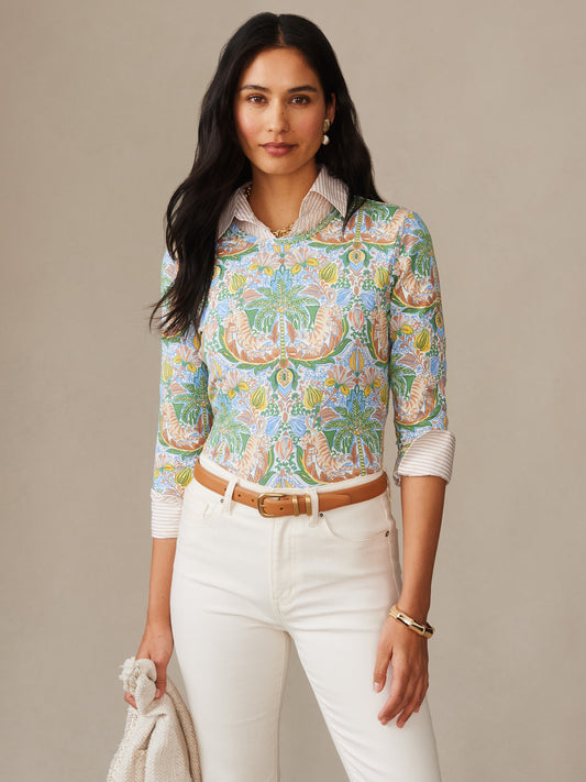 Woman wearing the Signature Tee in Tigress Tropico by J.McLaughlin, featuring an intricate green, blue, and brown pattern with a classic fit, styled with white pants and a tan belt, showcasing effortlessly stylish, enduring designs crafted with innovative fabrics for a legacy of timeless fashion. A destination for defining style. Life, Well-Lived.