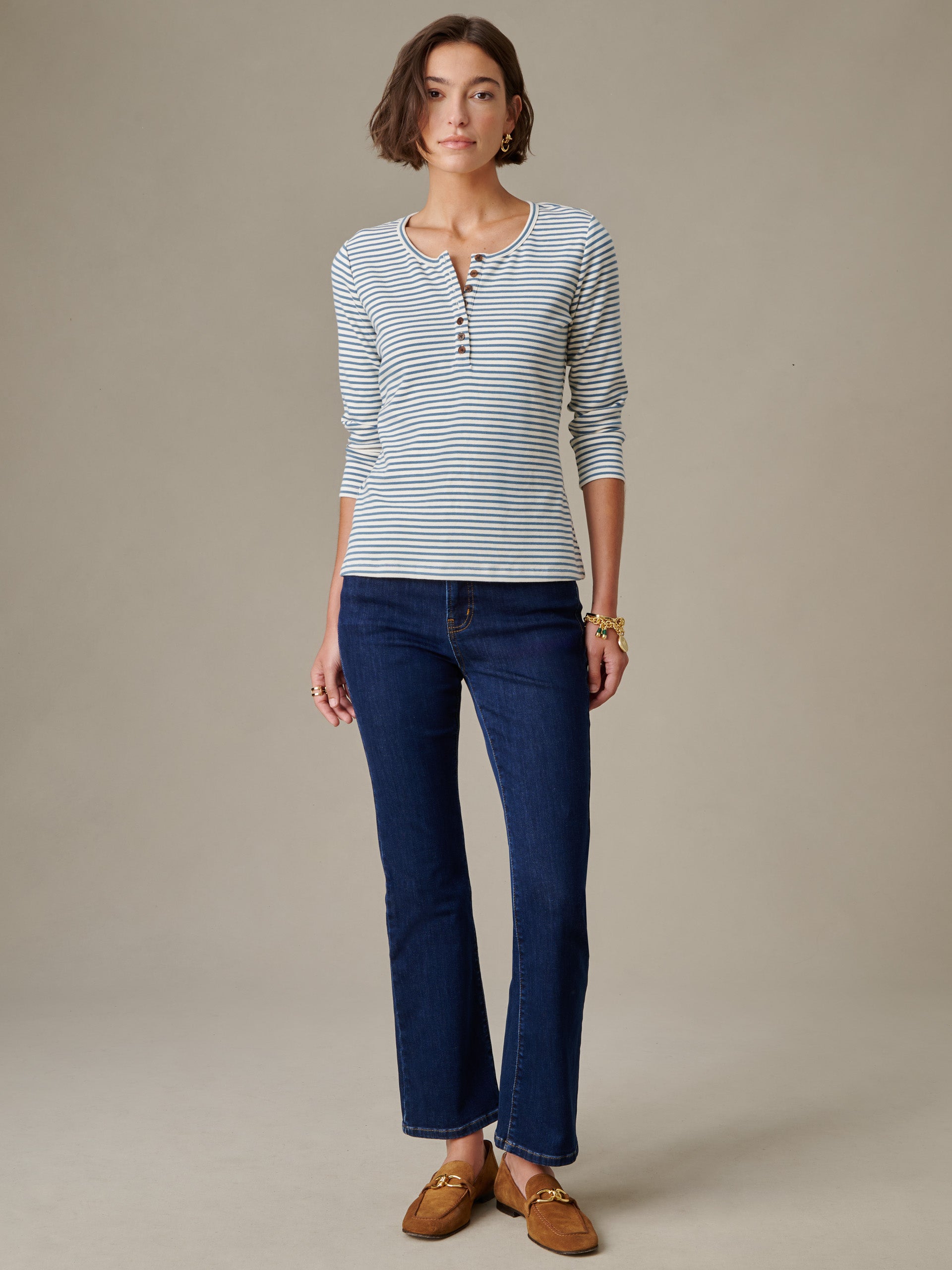 Woman wearing J.McLaughlin Sinclair Henley in Stripe top paired with dark blue jeans and brown loafers, showcasing effortlessly stylish and enduring designs.
