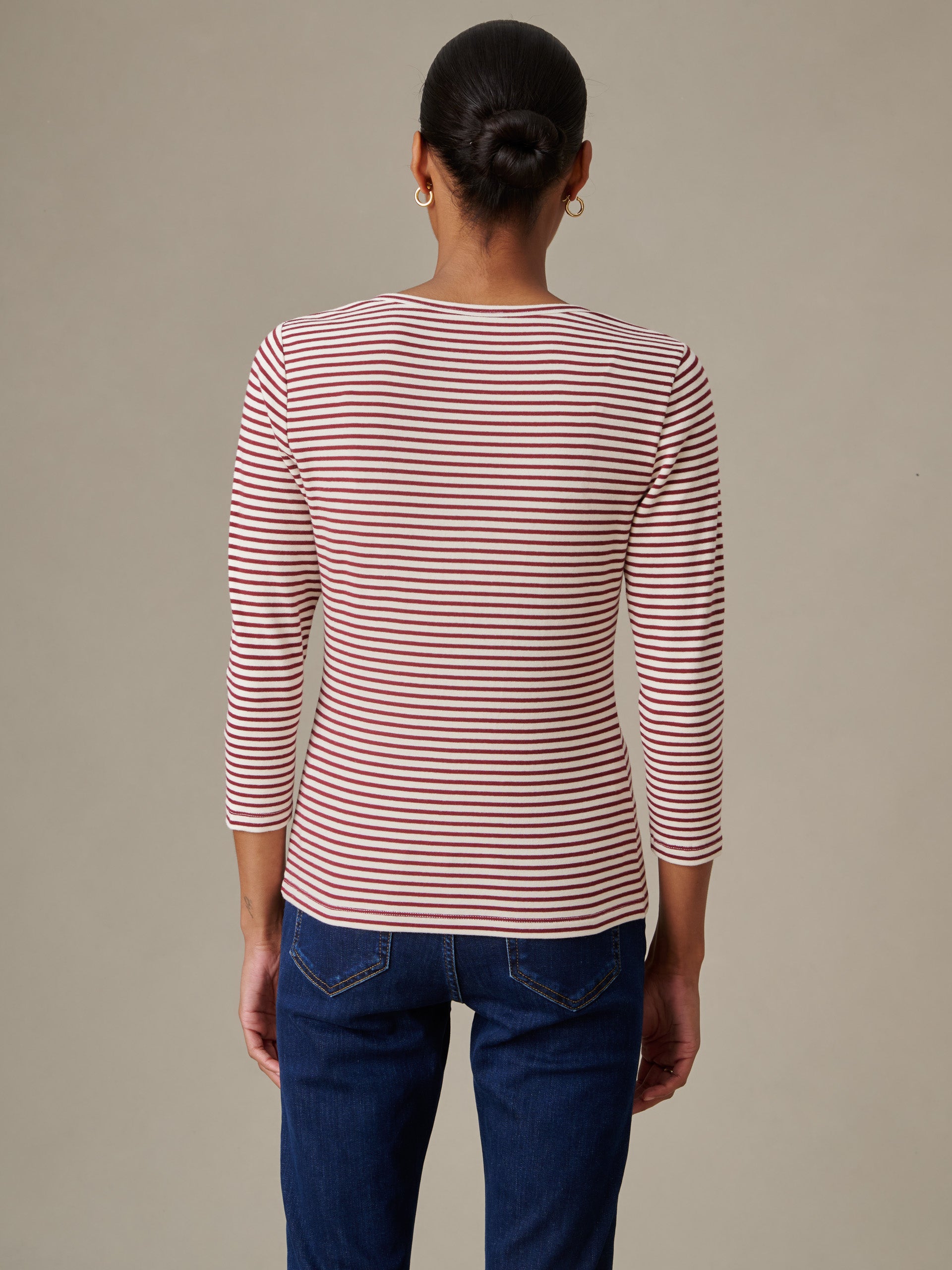 Woman wearing a red and white striped Sinclair Henley in Stripe from J.McLaughlin, paired with dark blue jeans, showcasing timeless style and impeccable craftsmanship.