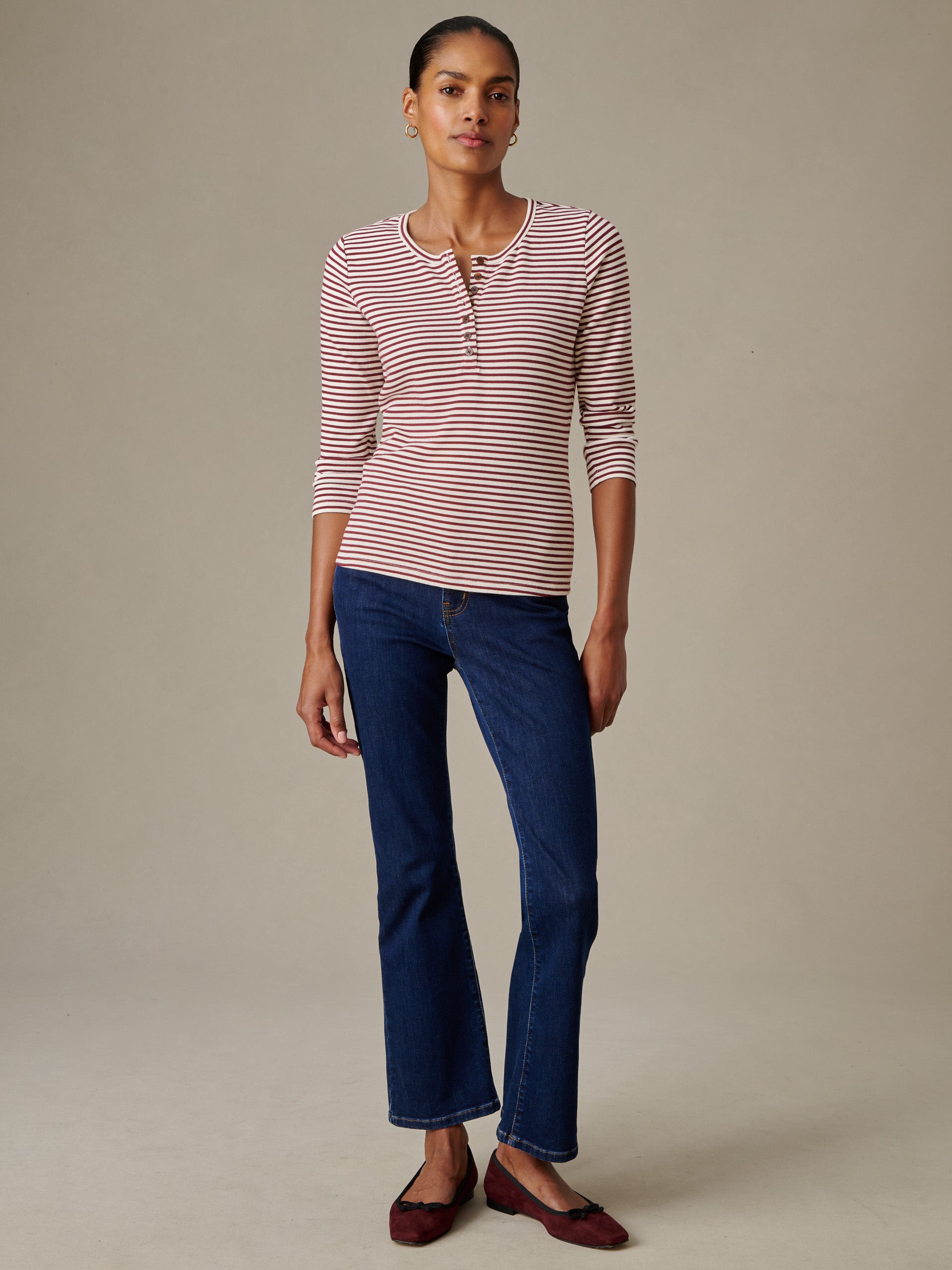 Woman wearing a Sinclair Henley in Stripe by J.McLaughlin with three-quarter sleeves and button detail, paired with dark blue jeans and maroon flats, showcasing timeless style.