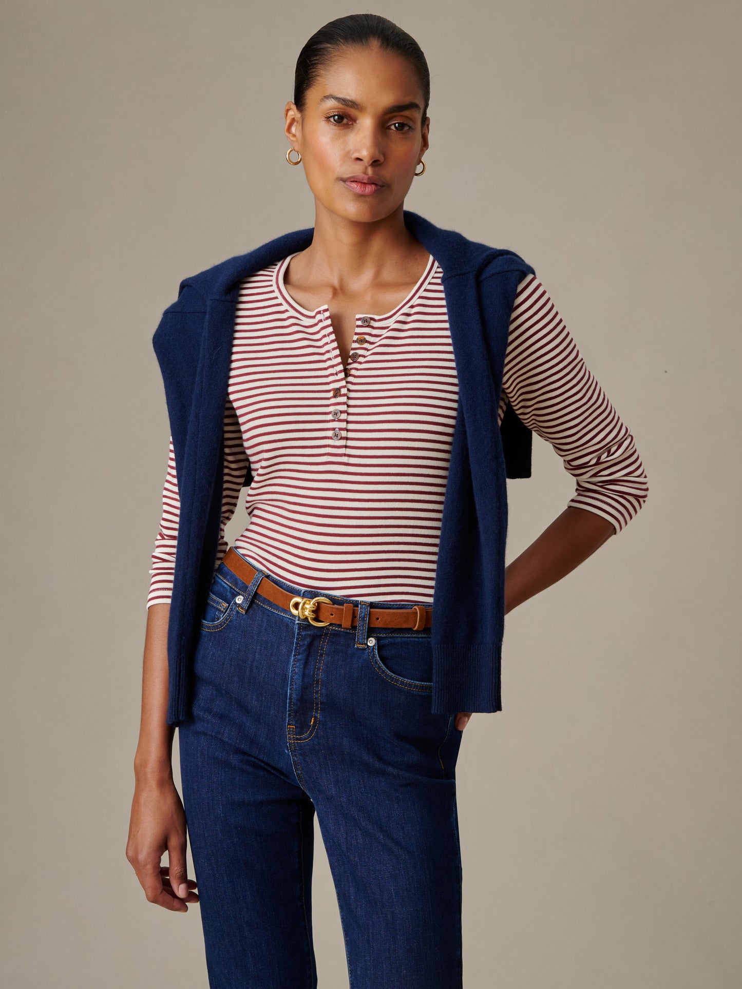 Model wearing a Sinclair Henley in Stripe with a navy sweater draped over shoulders paired with dark blue jeans and a brown belt, showcasing J.McLaughlin’s timeless style.