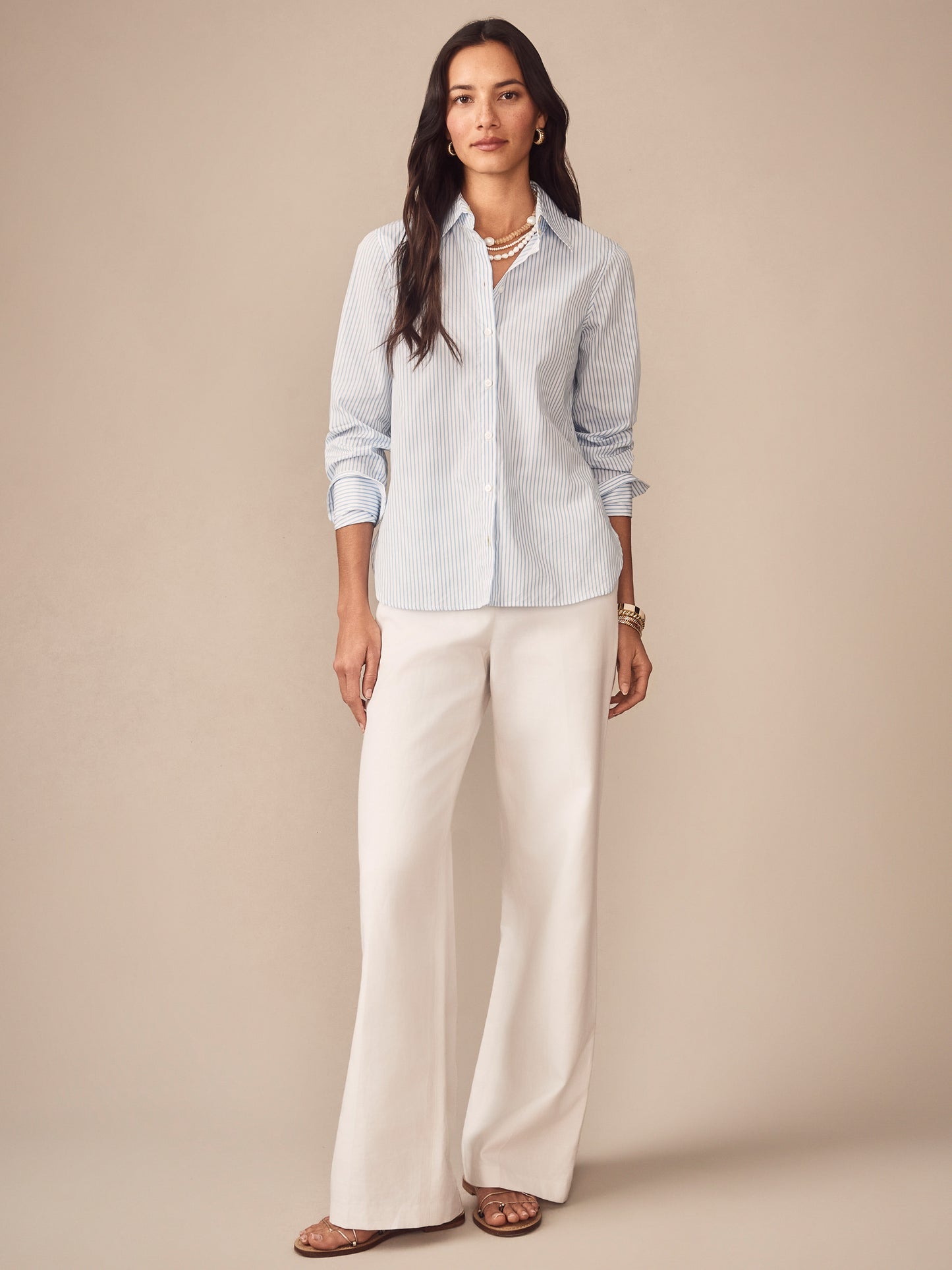 Woman wearing a Sloane Shirt in Stripe by J.McLaughlin with light blue and white stripes, paired with white wide-leg pants, embodying effortlessly stylish, enduring designs and innovative fabrics. A destination for defining style. Life, Well-Lived.
