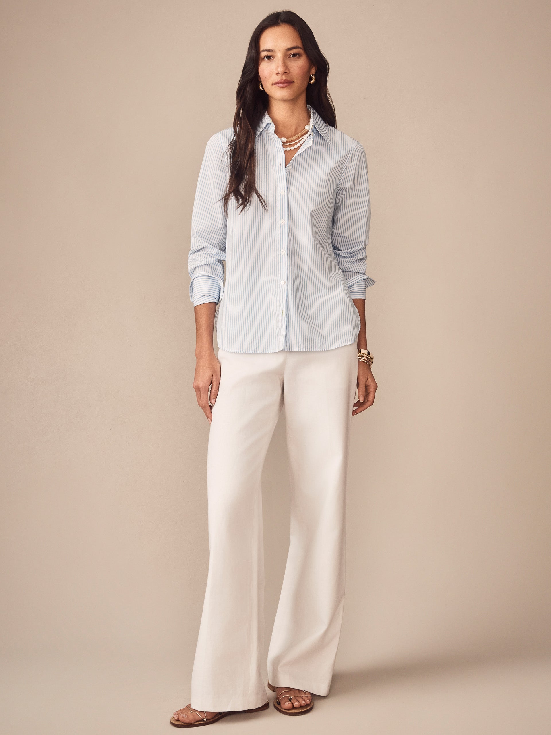 Woman wearing a Sloane Shirt in Stripe by J.McLaughlin with light blue and white stripes, paired with white wide-leg pants, embodying effortlessly stylish, enduring designs and innovative fabrics. A destination for defining style. Life, Well-Lived.